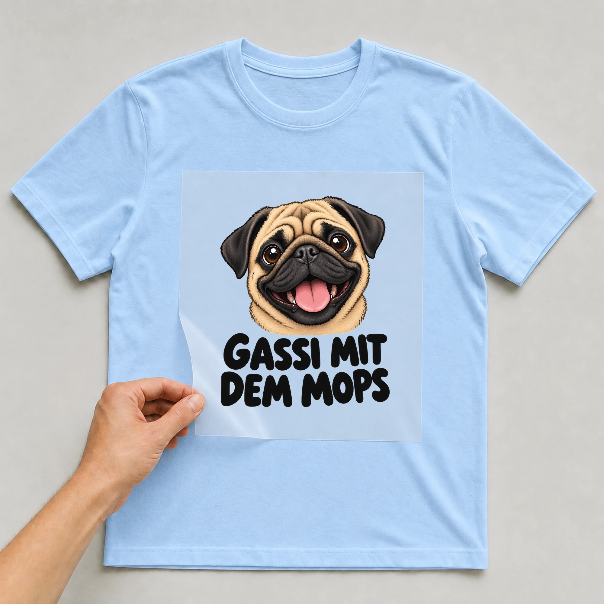 Bügelbild „Gassi mit dem Mops“ auf babyblauem T-Shirt, Folie wird aufgelegt