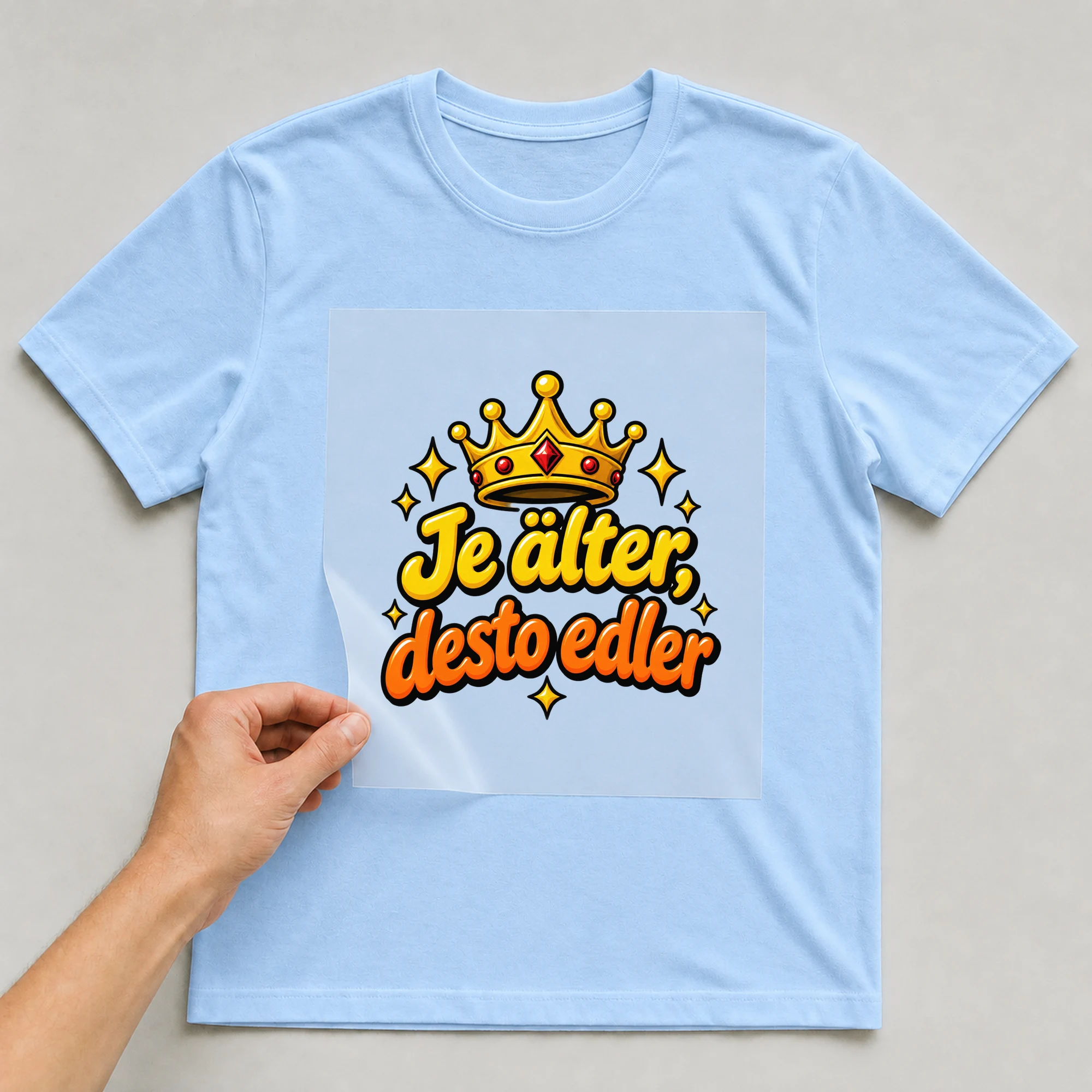 Bügelbild „Je älter, desto edler“ auf babyblauem T-Shirt, Folie wird aufgelegt