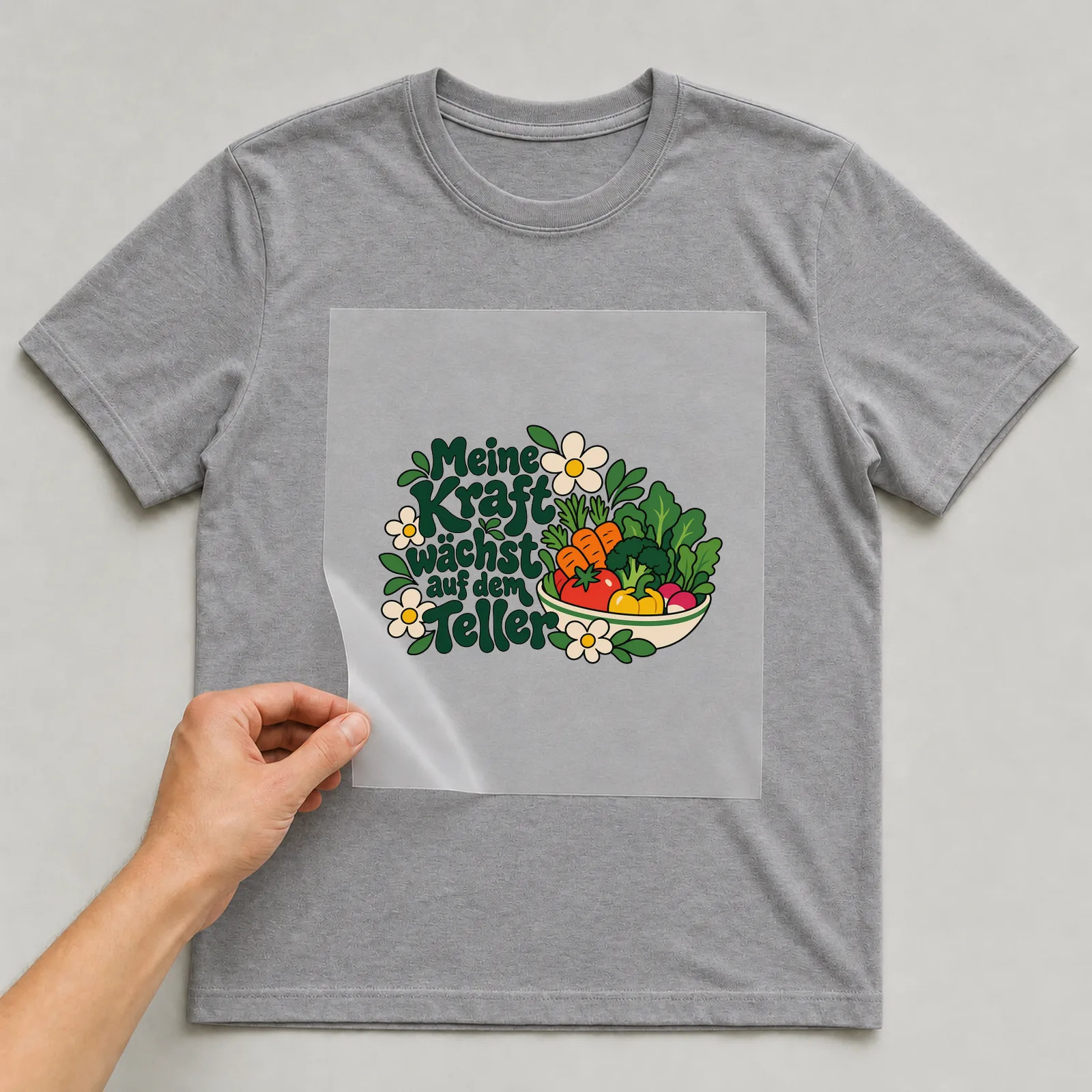 Bügelbild „Meine Kraft wächst auf dem Teller“ auf grauem T-Shirt, Folie wird aufgelegt