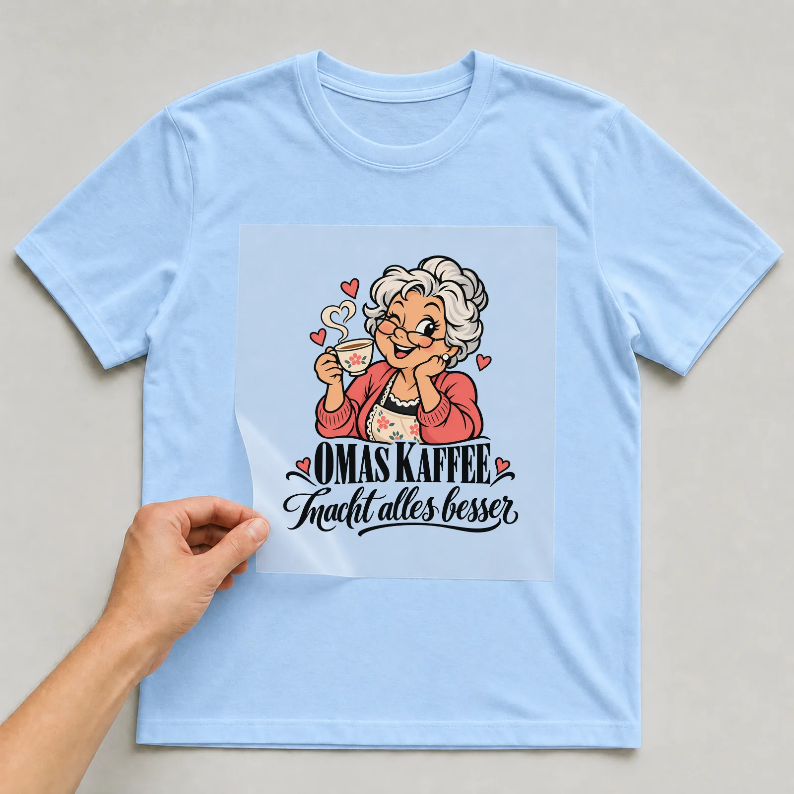 Bügelbild „Omas Kaffee macht alles besser“ auf hellblauem T-Shirt, Folie wird aufgelegt