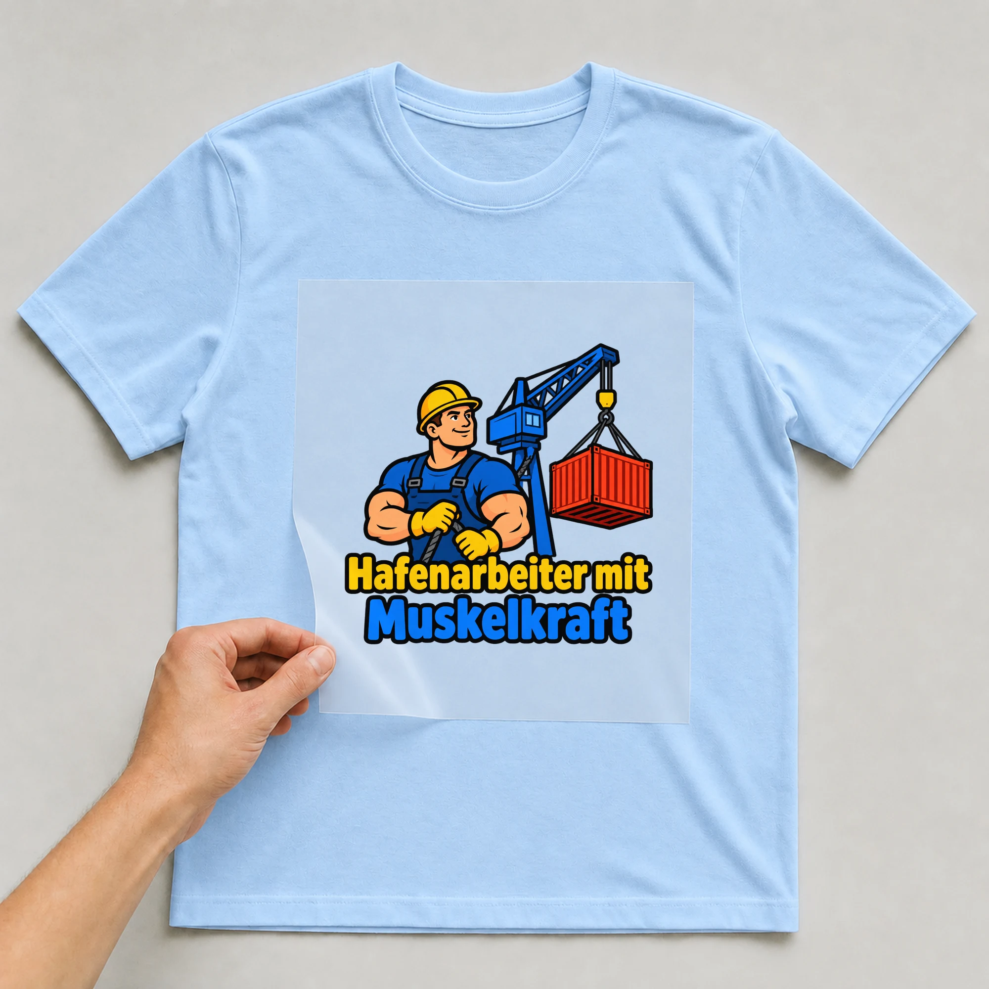 Bügelbild „Hafenarbeiter mit Muskelkraft“ auf babyblauem T-Shirt, Folie wird aufgelegt