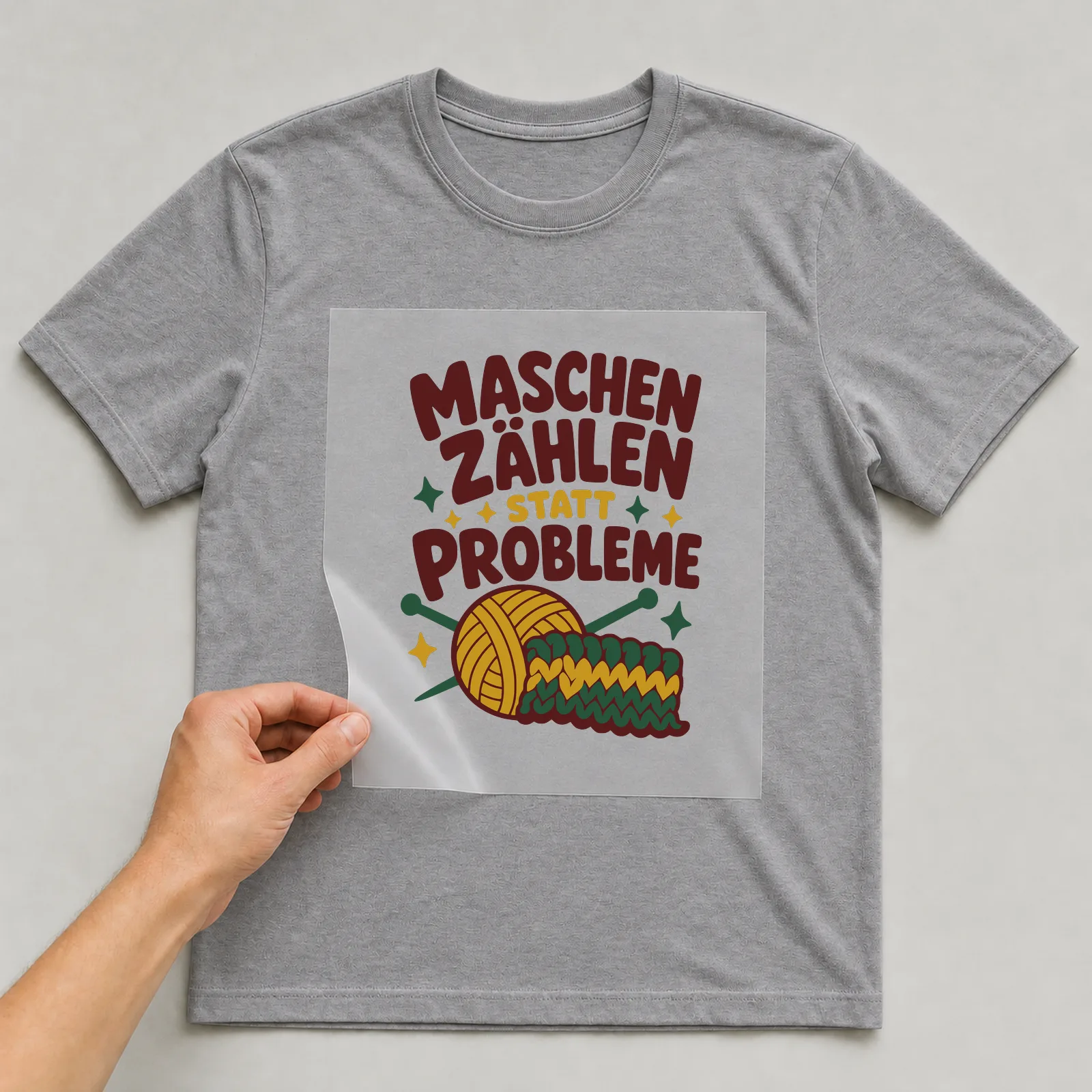 Bügelbild Maschen zählen statt Probleme auf grauem T-Shirt, Folie wird aufgelegt