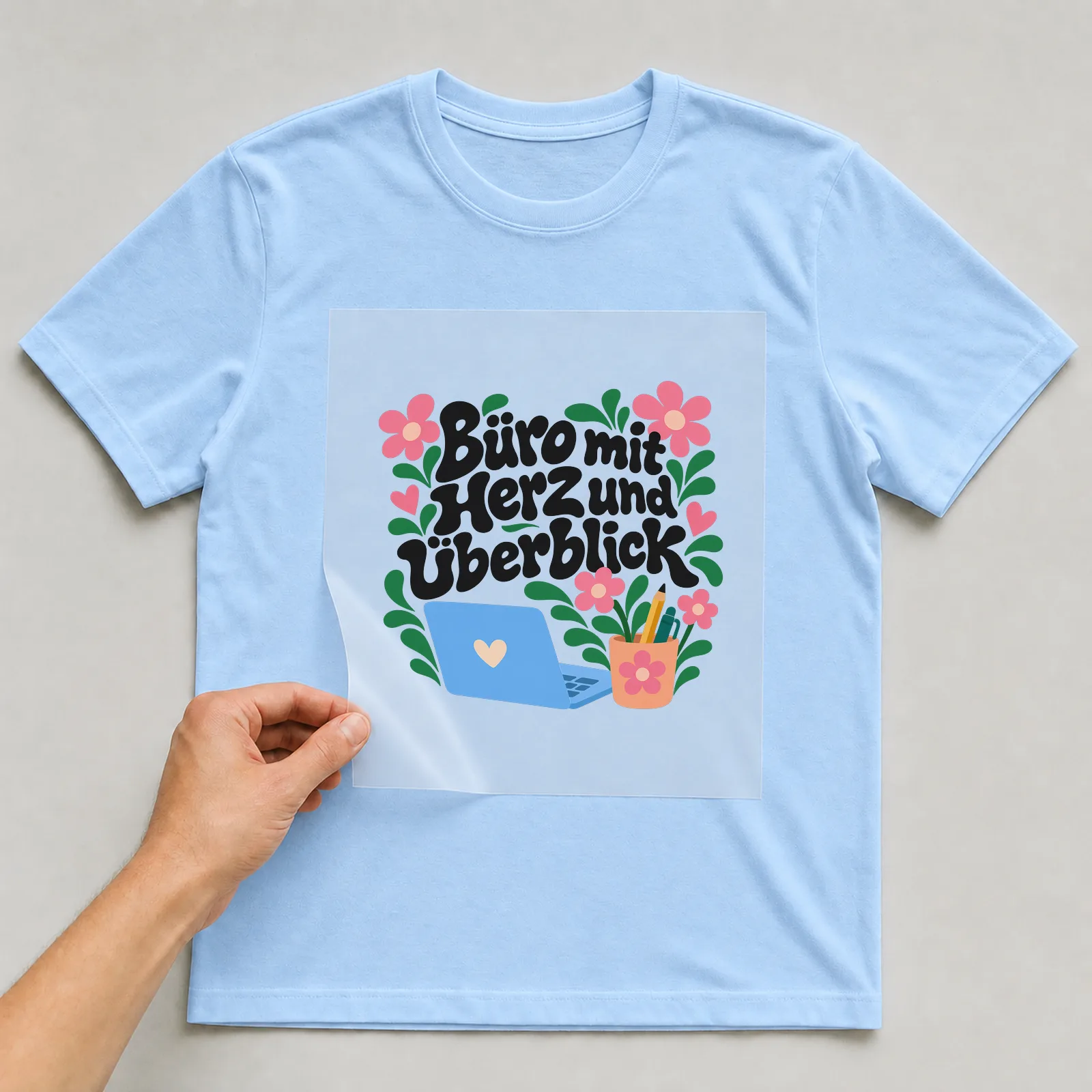 Bügelbild „Büro mit Herz und Überblick“ auf hellblauem T-Shirt, Folie wird aufgelegt