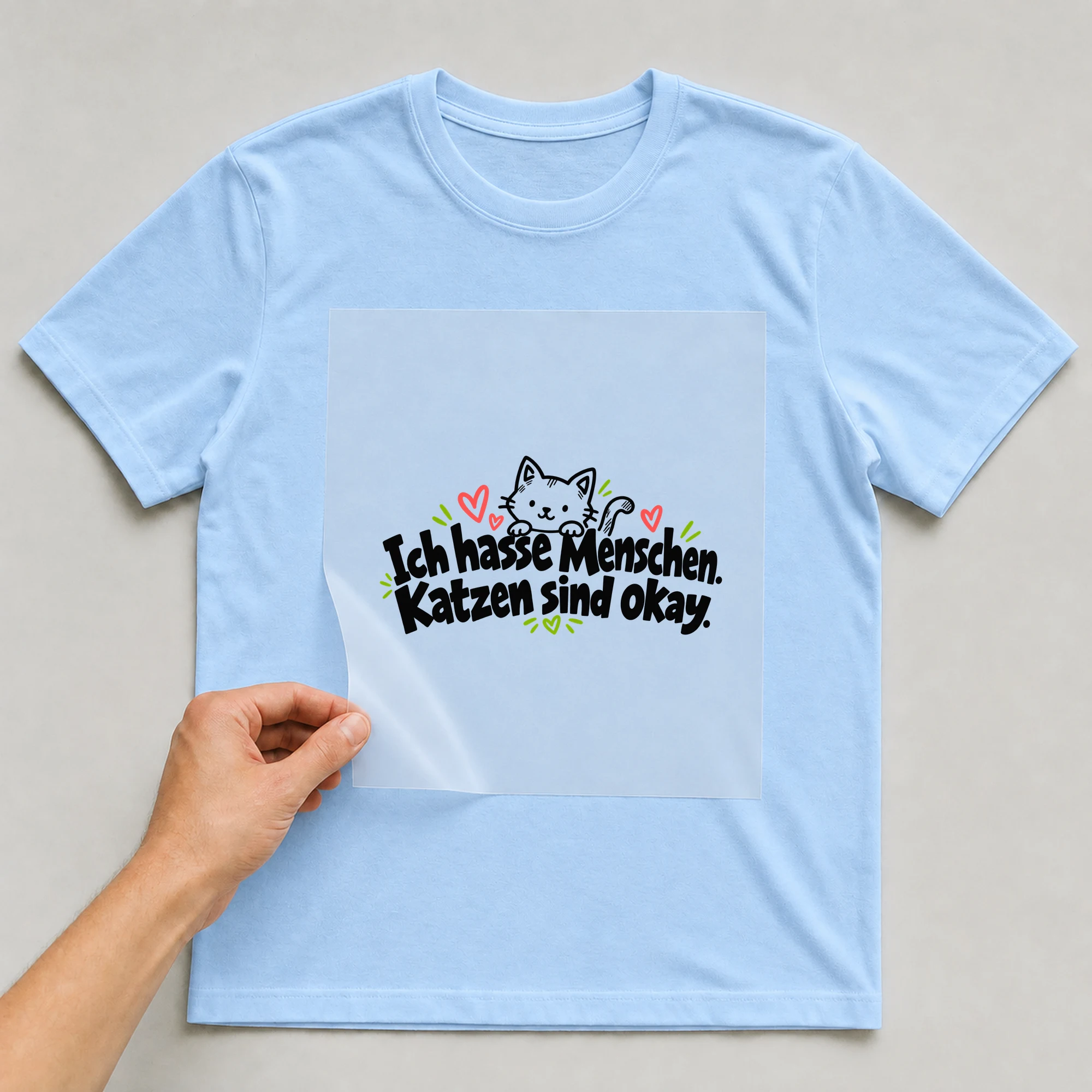 Bügelbild „Ich hasse Menschen. Katzen sind okay.“ auf babyblauem T-Shirt, Folie wird aufgelegt