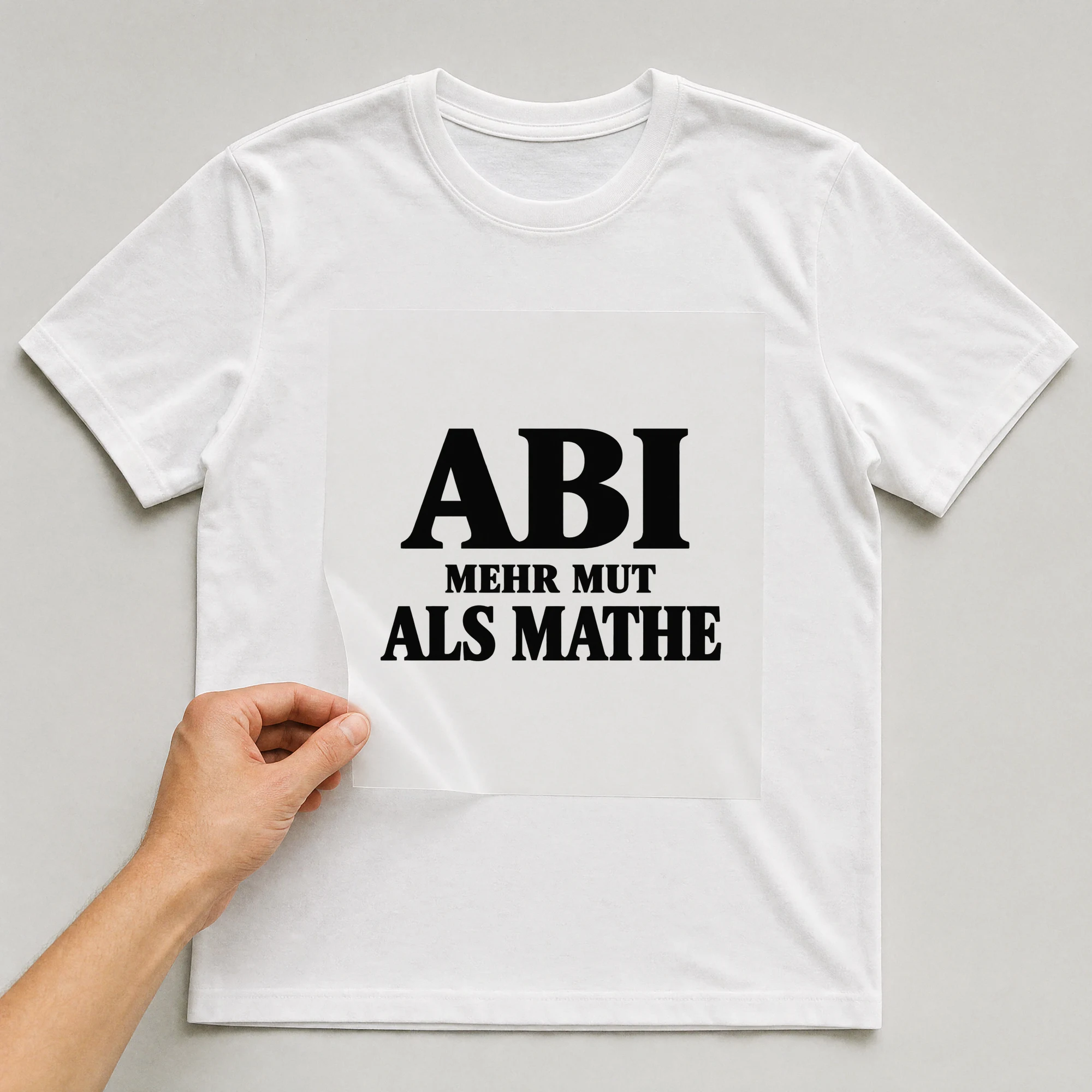 Bügelbild „Abi: Mehr Mut als Mathe“ auf weißem T-Shirt, Folie wird aufgelegt