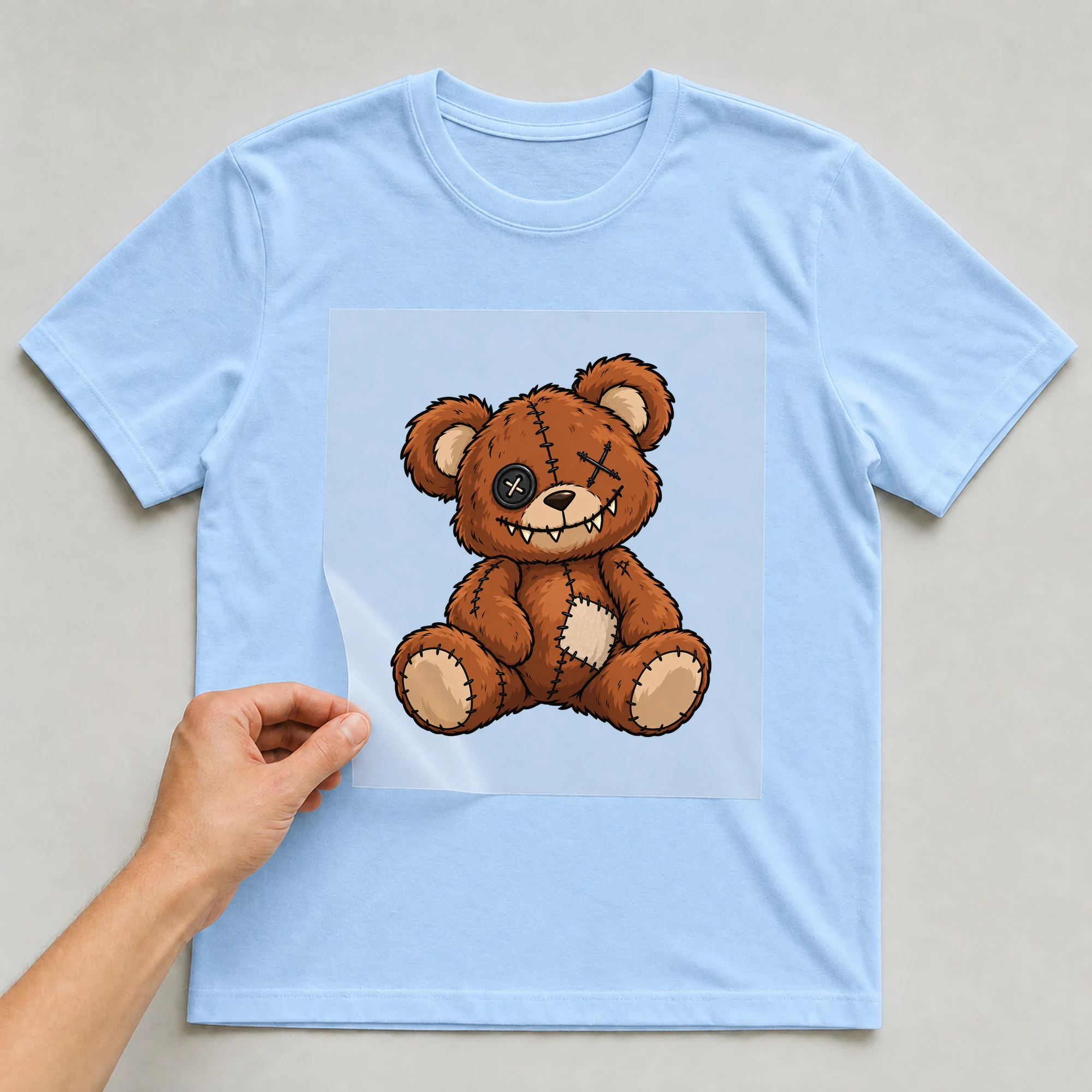 Bügelbild „Horrorteddy“ auf babyblauem T-Shirt, Folie wird aufgelegt