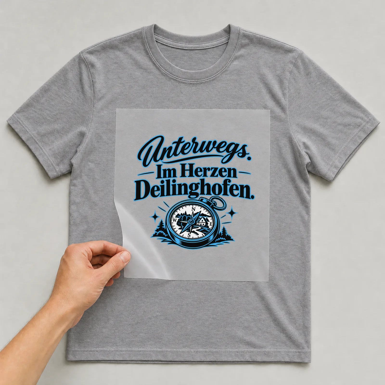 Bügelbild „Unterwegs. Im Herzen Deilinghofen.“ auf grauem T-Shirt, Folie wird aufgelegt
