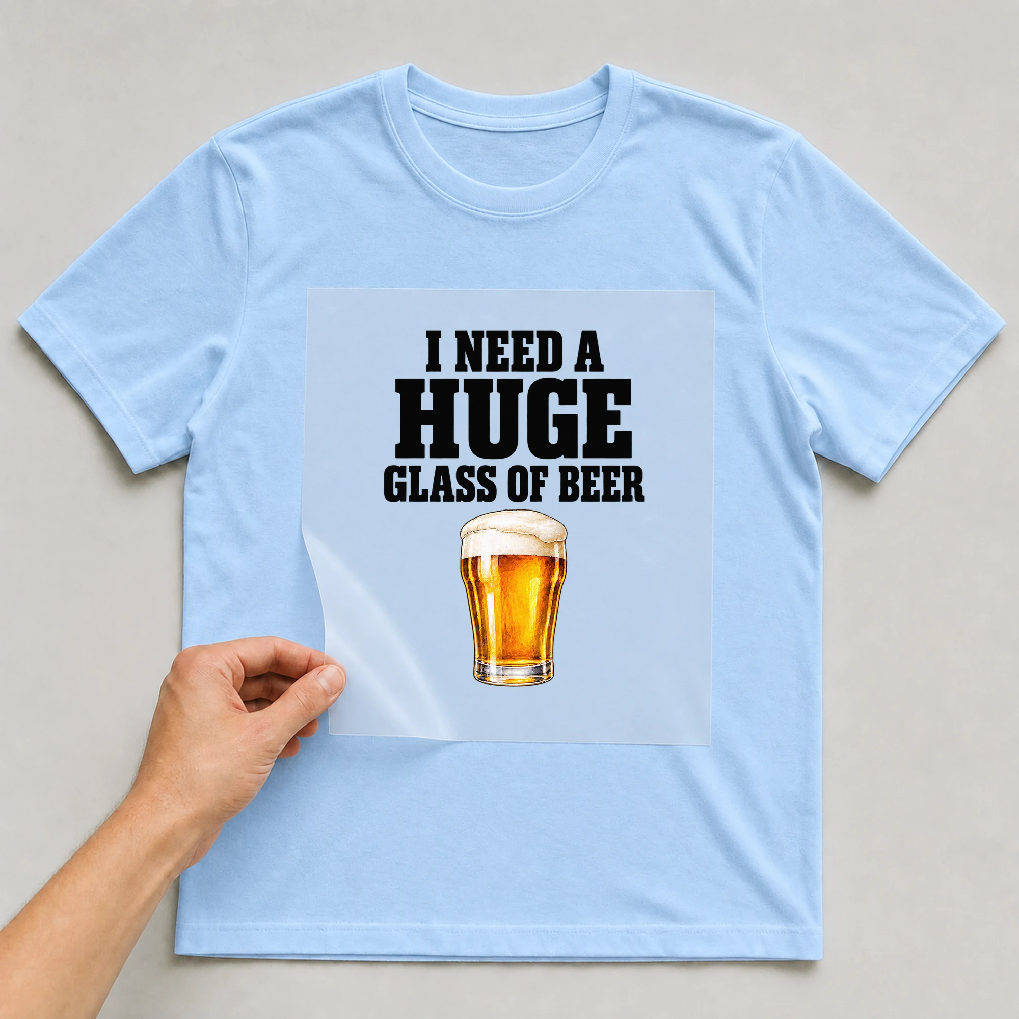 Bügelbild „I Need A Huge Glass Of Beer“ auf babyblauem T-Shirt, Folie wird aufgelegt