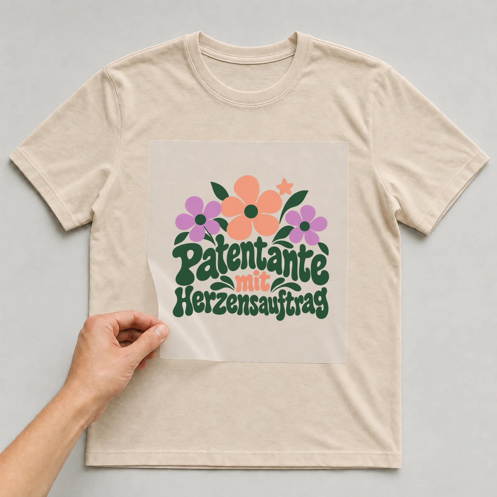 Bügelbild „Patentante mit Herzensauftrag“ auf beigem T-Shirt, Folie wird aufgelegt