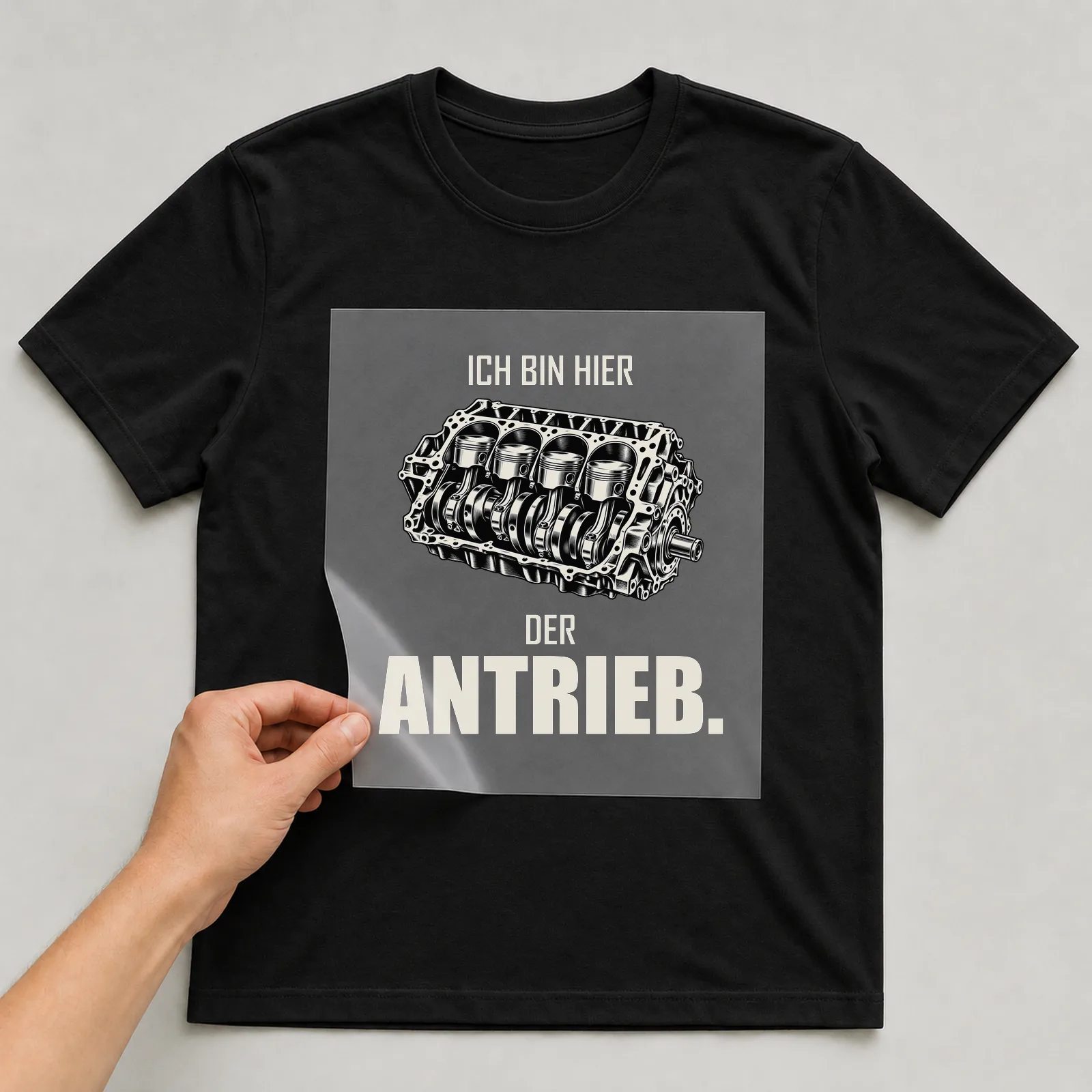 Bügelbild „Ich bin hier der Antrieb“ auf schwarzem T-Shirt, Folie wird aufgelegt