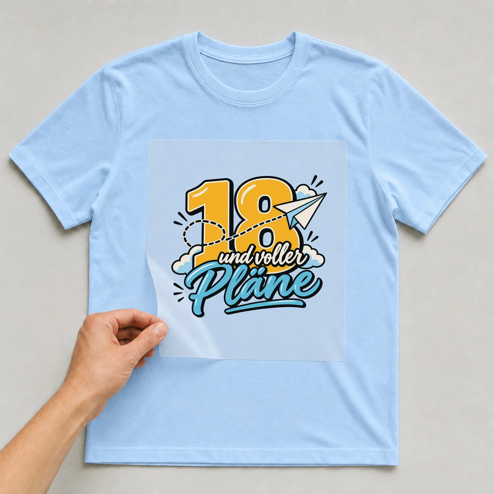Bügelbild „18 und voller Pläne“ auf hellblauem T-Shirt, Folie wird aufgelegt