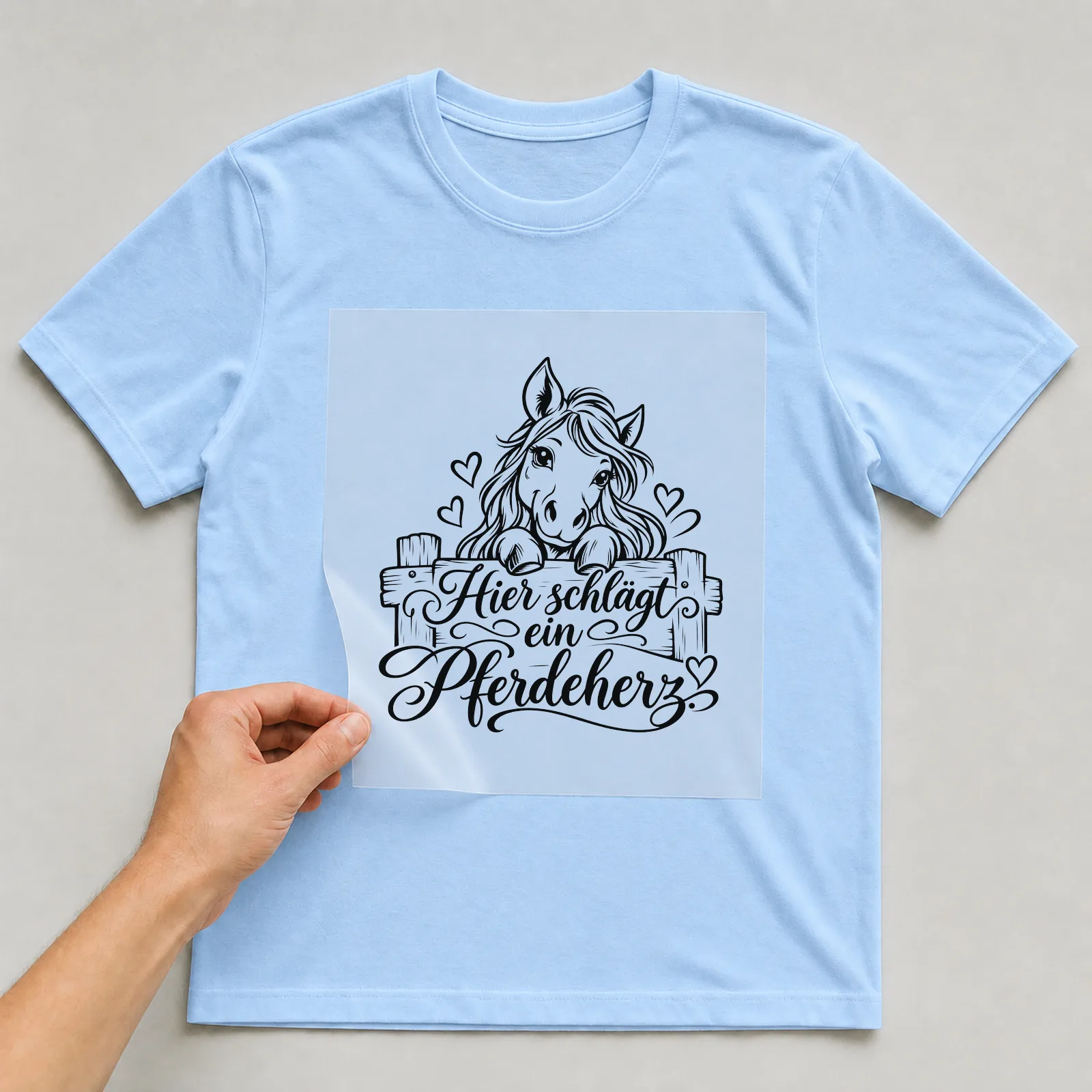 Bügelbild „Hier schlägt ein Pferdeherz“ auf hellblauem T-Shirt, Folie wird aufgelegt
