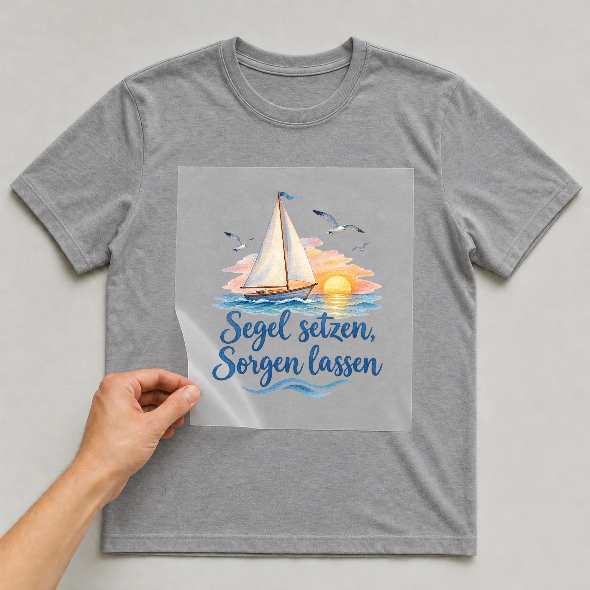 Bügelbild „Segel setzen, Sorgen lassen“ auf grauem T-Shirt, Folie wird aufgelegt