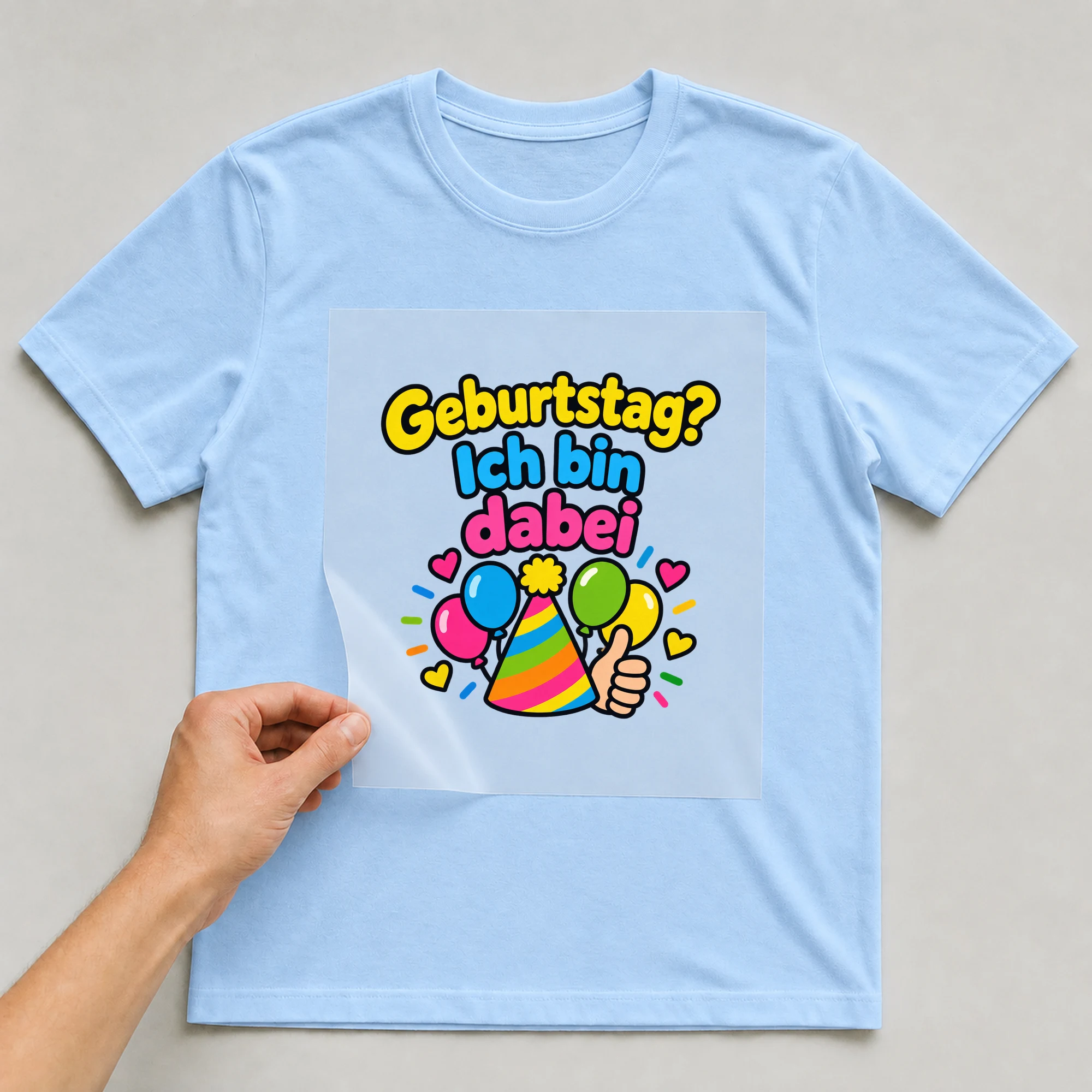 Bügelbild „Geburtstag? Ich bin dabei“ auf babyblauem T-Shirt, Folie wird aufgelegt