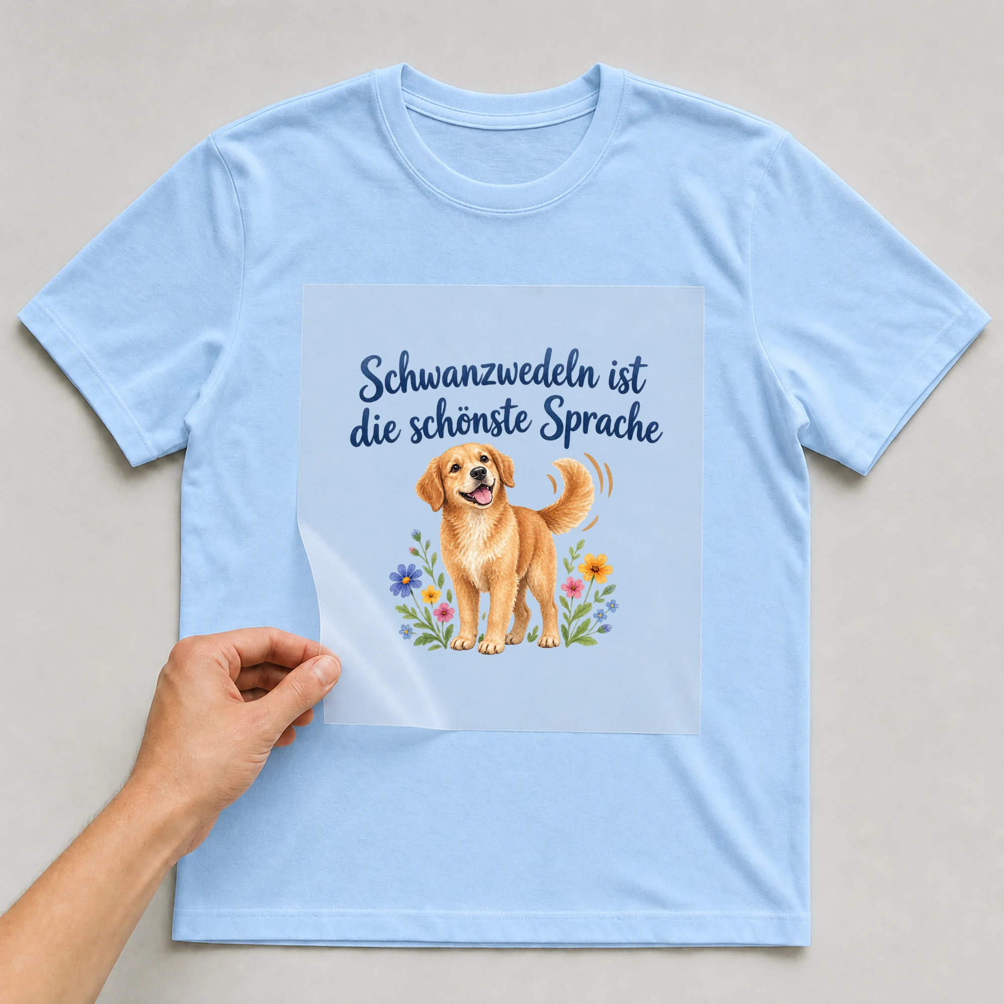 Bügelbild „Schwanzwedeln ist die schönste Sprache“ auf babyblauem T-Shirt, Folie wird aufgelegt