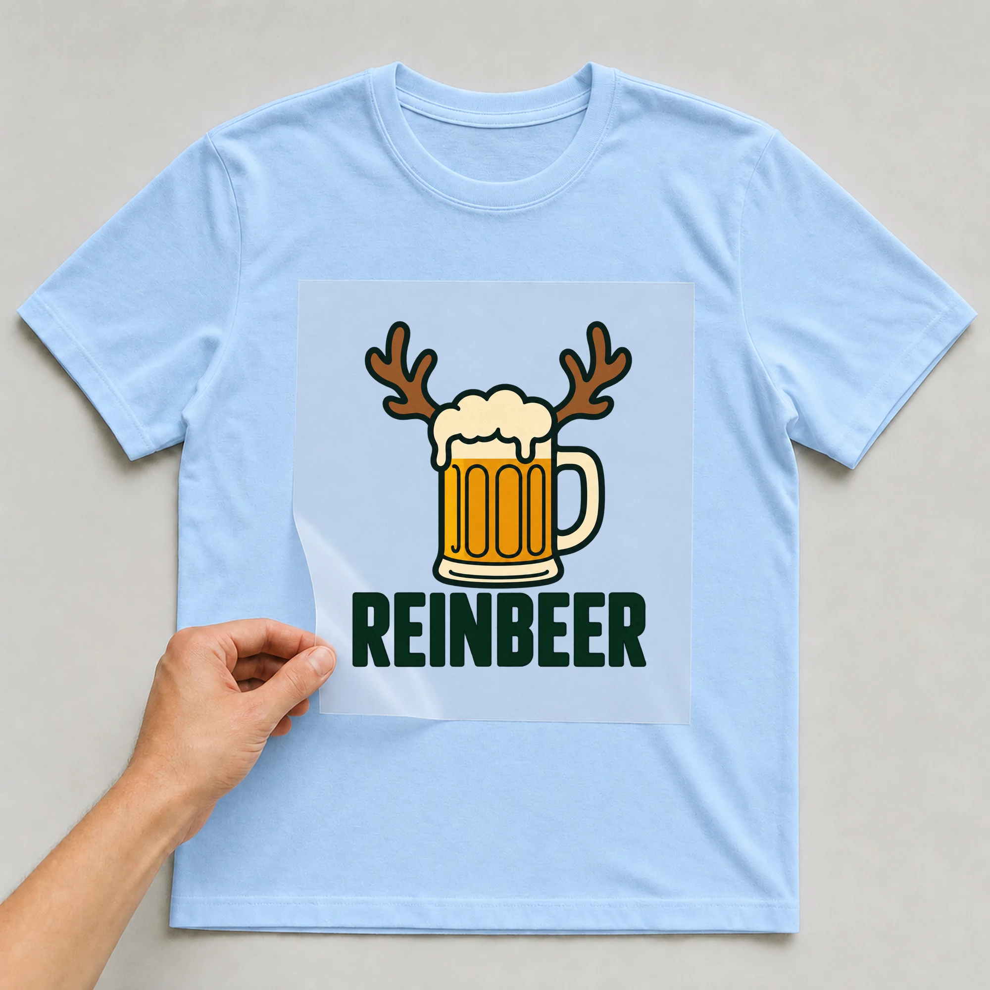 Bügelbild „Reinbeer“ auf babyblauem T-Shirt, Folie wird aufgelegt