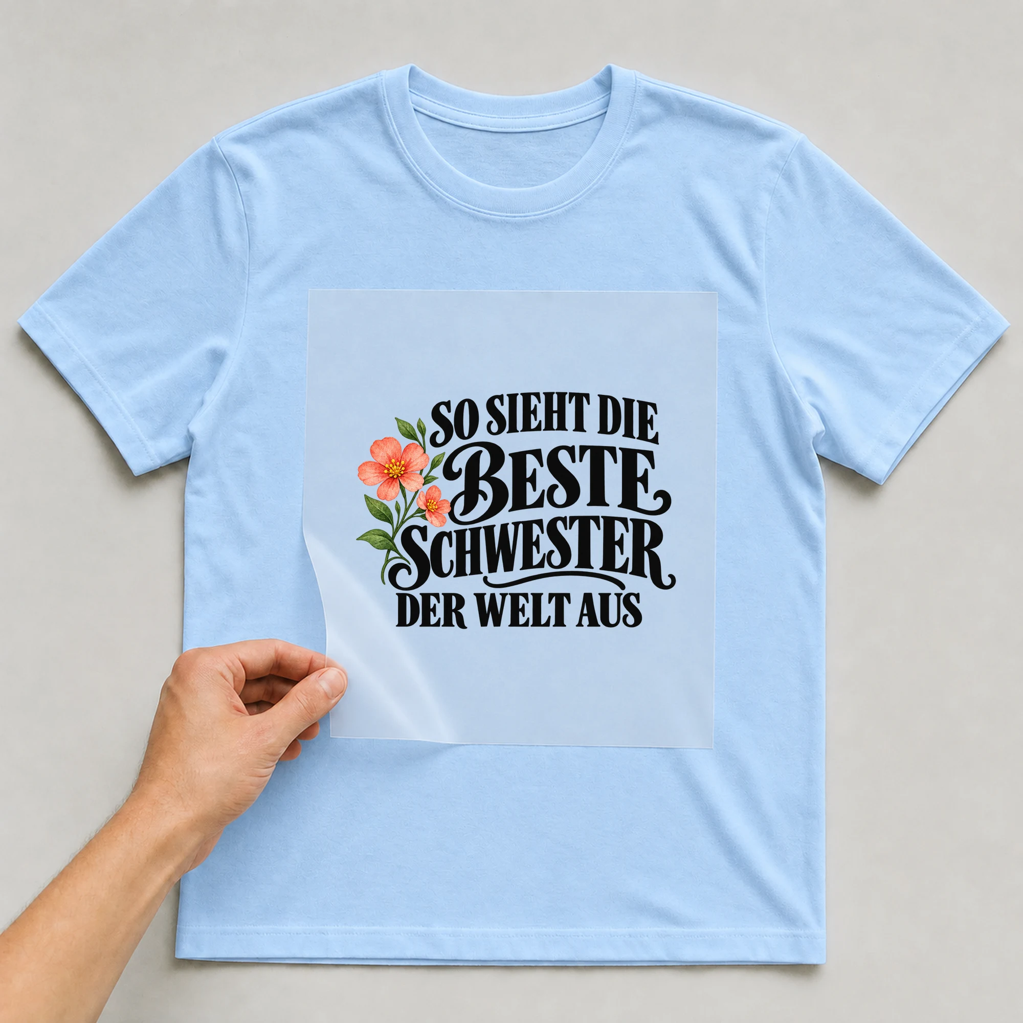 Bügelbild „So sieht die beste Schwester der Welt aus“ auf babyblauem T-Shirt, Folie wird aufgelegt