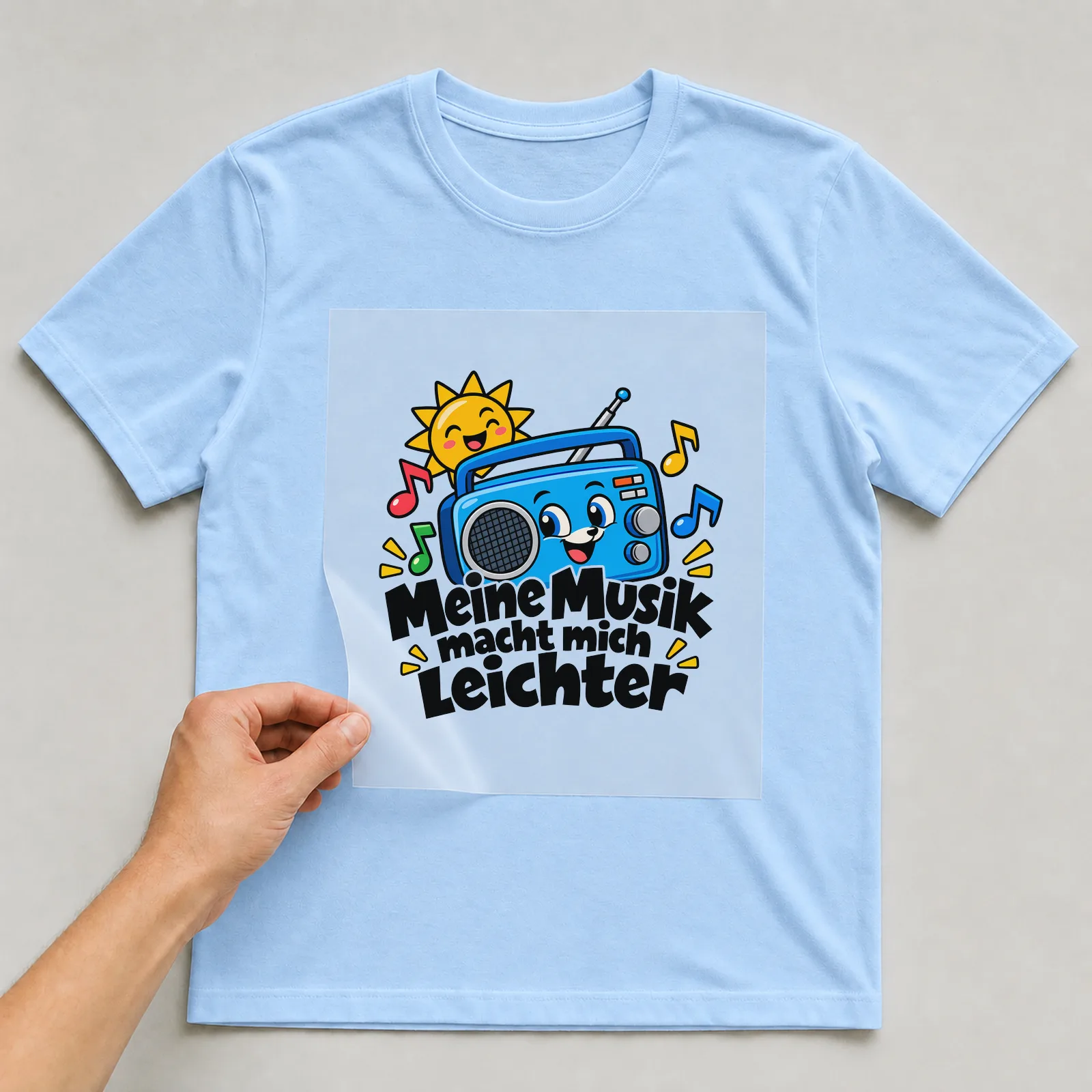 Bügelbild „Meine Musik macht mich leichter“ auf hellblauem T-Shirt, Folie wird aufgelegt