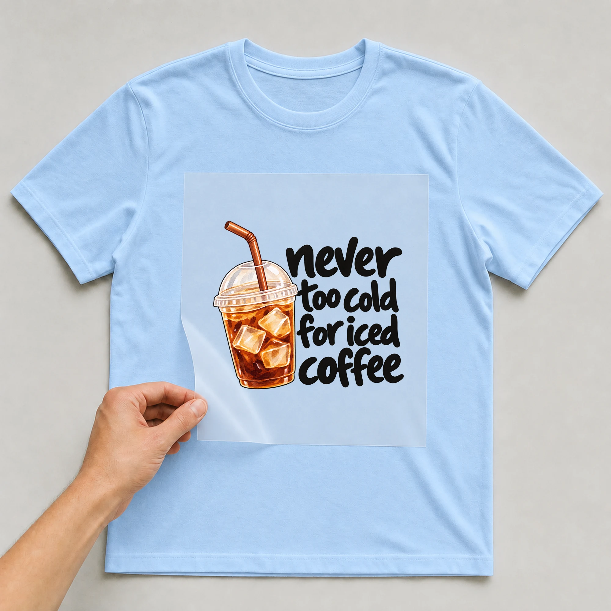 Bügelbild „never too cold for iced coffee“ auf babyblauem T-Shirt, Folie wird aufgelegt
