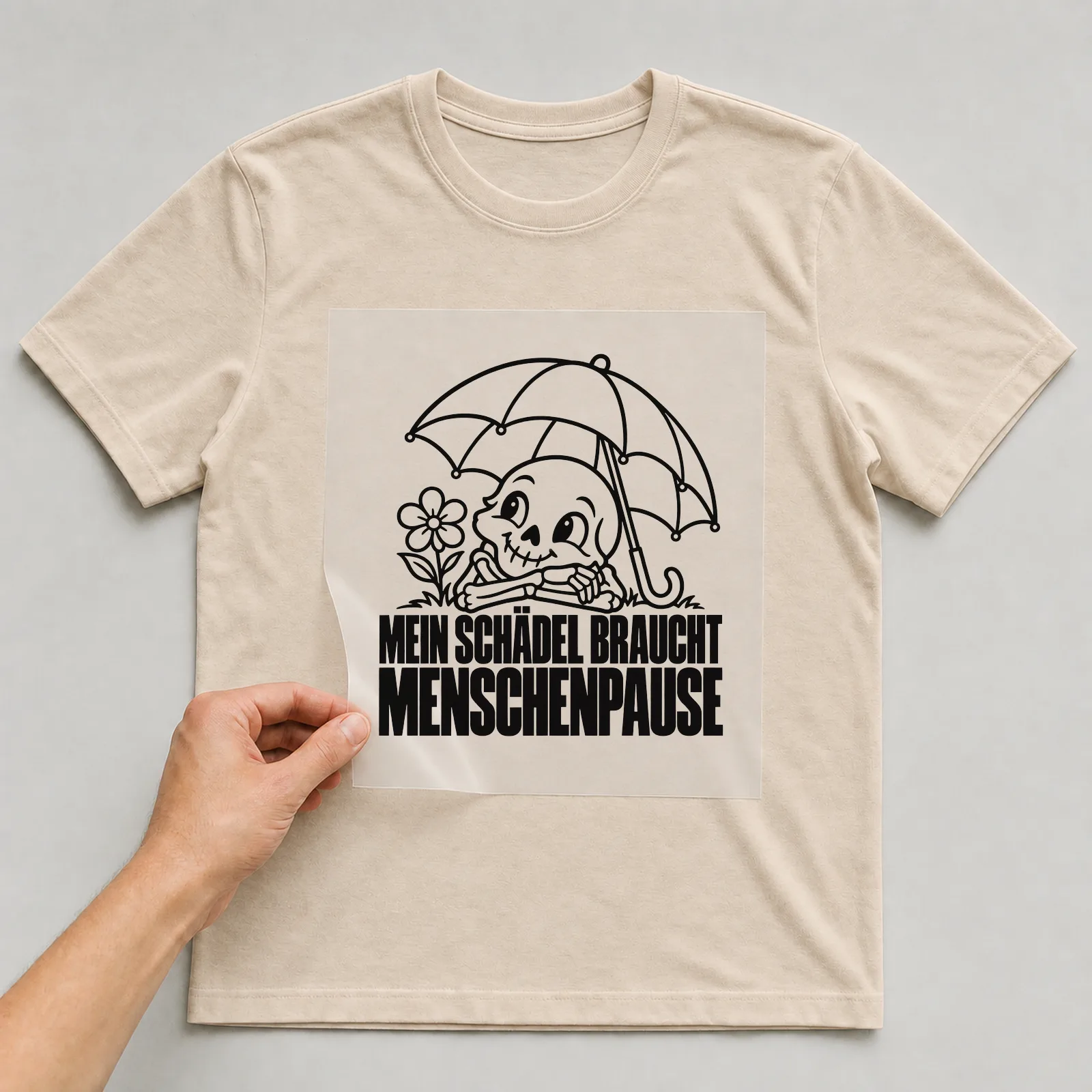 Bügelbild „Mein Schädel braucht Menschenpause“ auf beigem T-Shirt, Folie wird aufgelegt