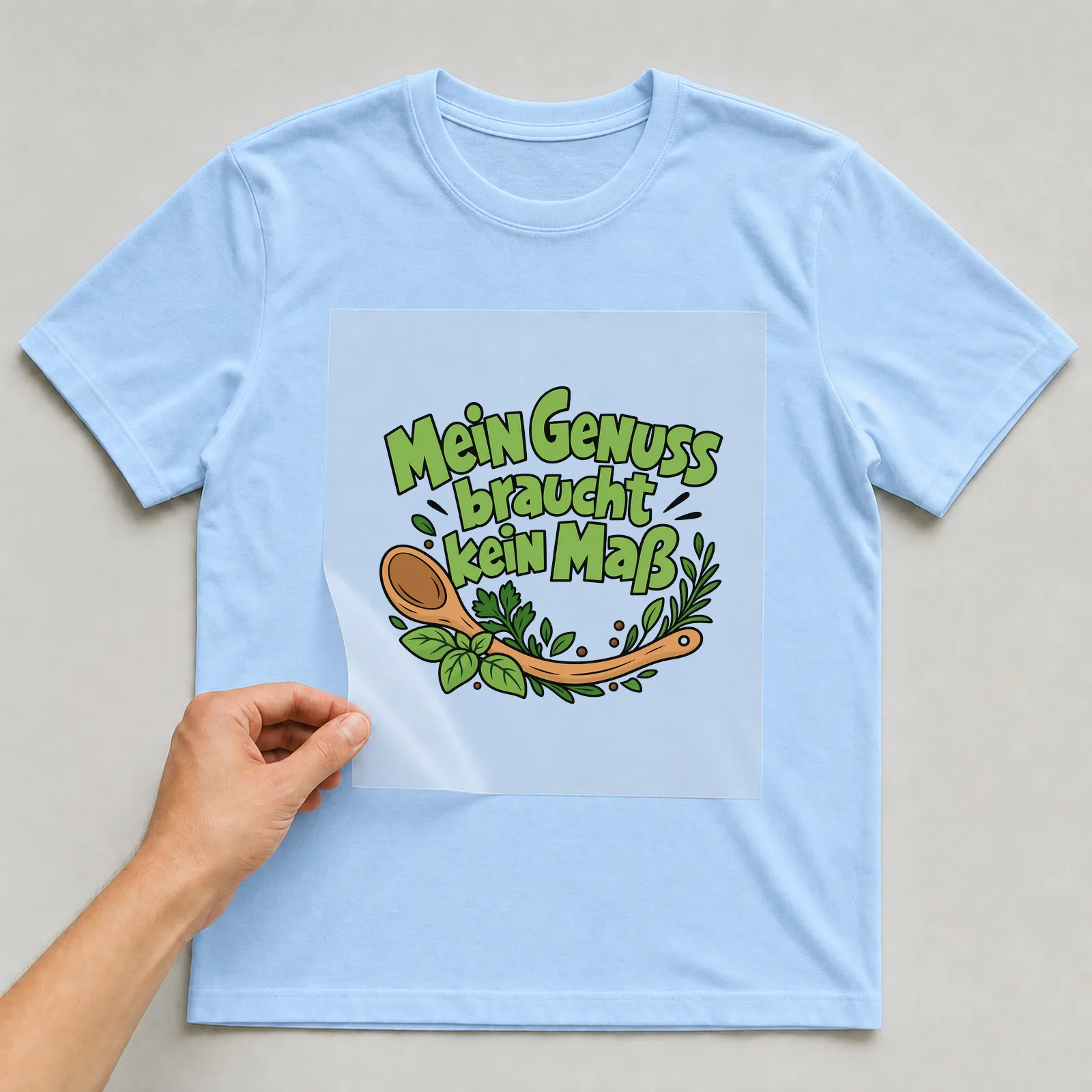 Bügelbild „Mein Genuss braucht kein Maß“ auf hellblauem T-Shirt, Folie wird aufgelegt