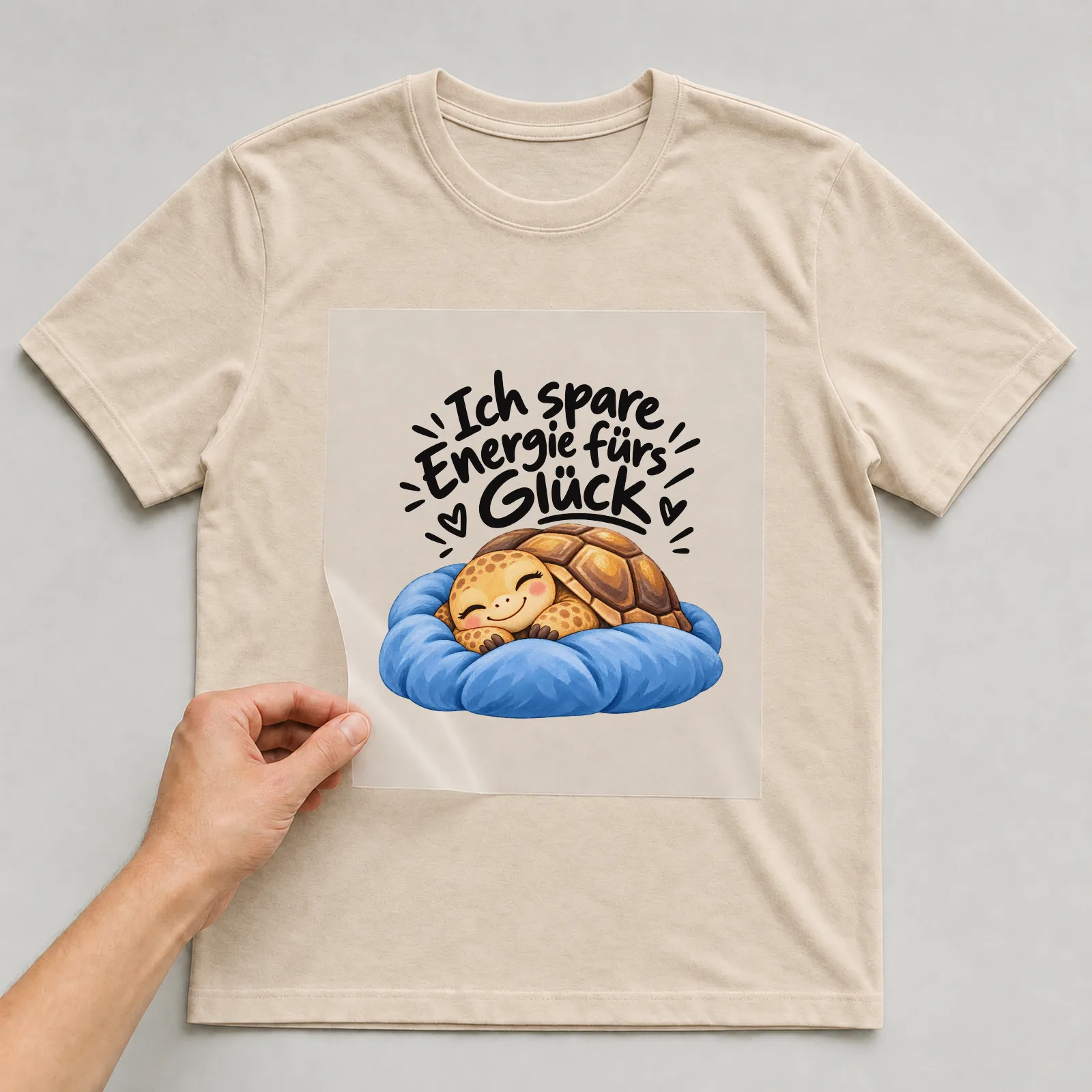 Bügelbild „Ich spare Energie fürs Glück“ auf beigem T-Shirt, Folie wird aufgelegt