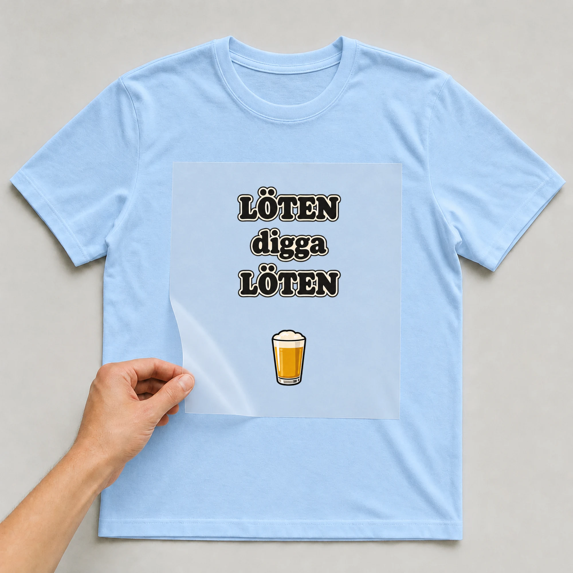 Bügelbild „LÖTEN digga LÖTEN“ auf babyblauem T-Shirt, Folie wird aufgelegt