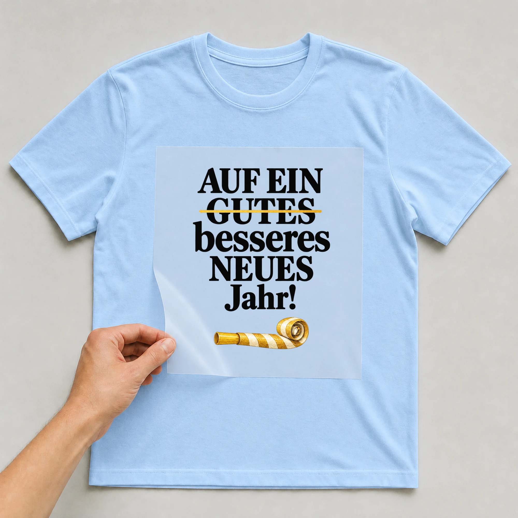 Bügelbild „Auf Ein Gutes Besseres Neues Jahr!“ auf babyblauem T-Shirt, Folie wird aufgelegt