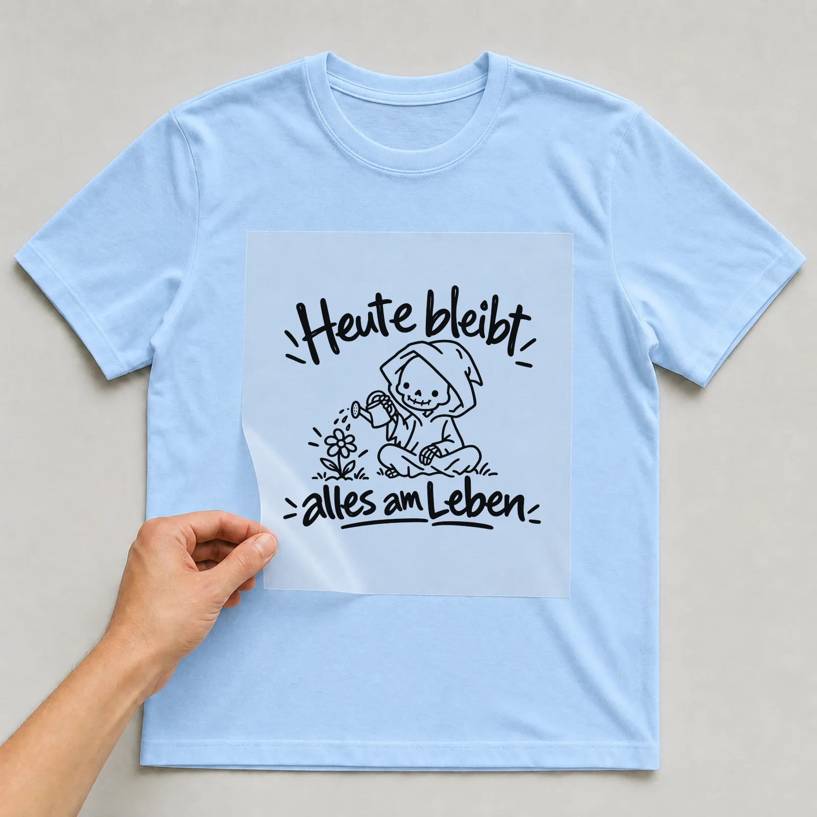 Bügelbild „Heute bleibt alles am Leben“ auf hellblauem T-Shirt, Folie wird aufgelegt