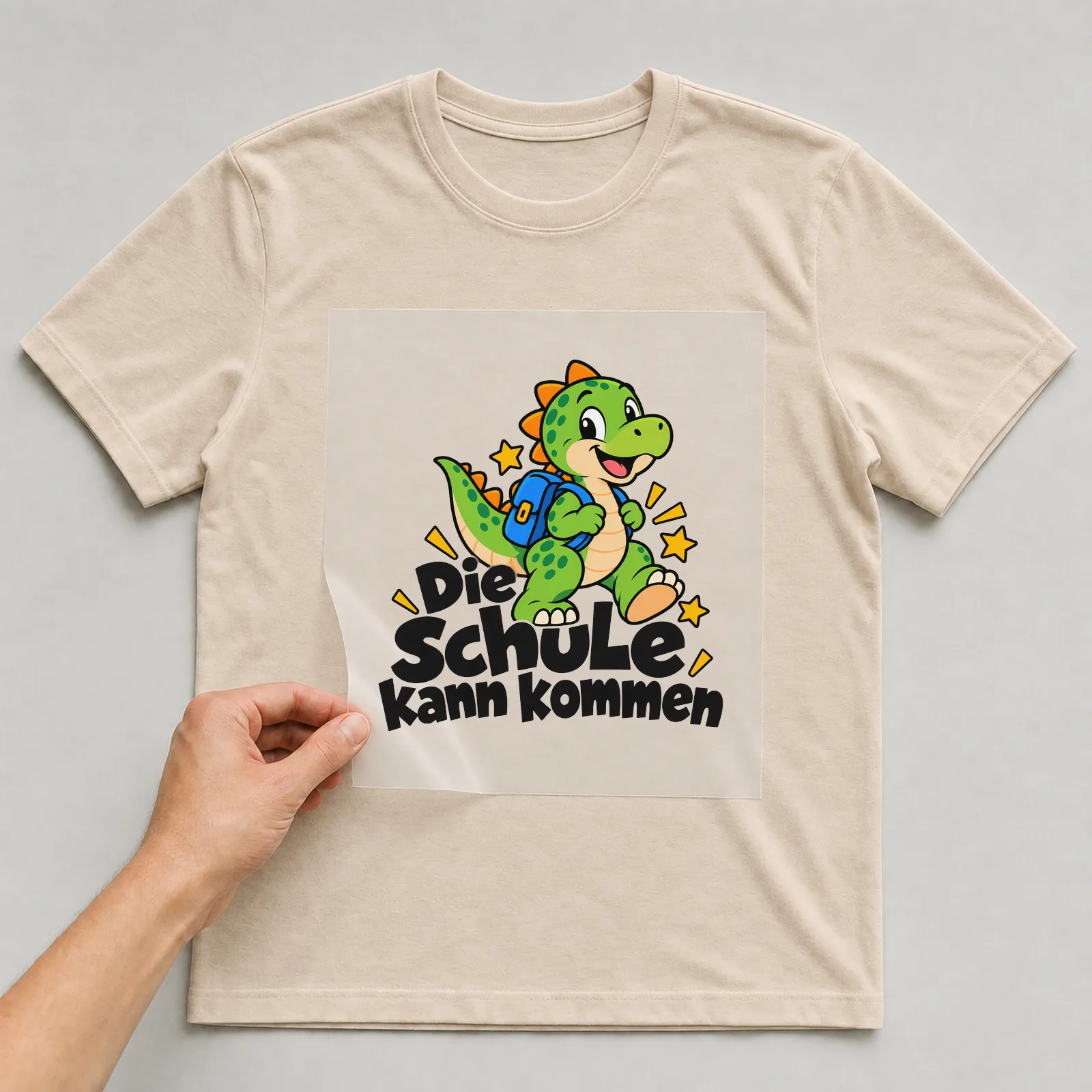 Bügelbild „Die Schule kann kommen“ auf beigem T-Shirt, Folie wird aufgelegt