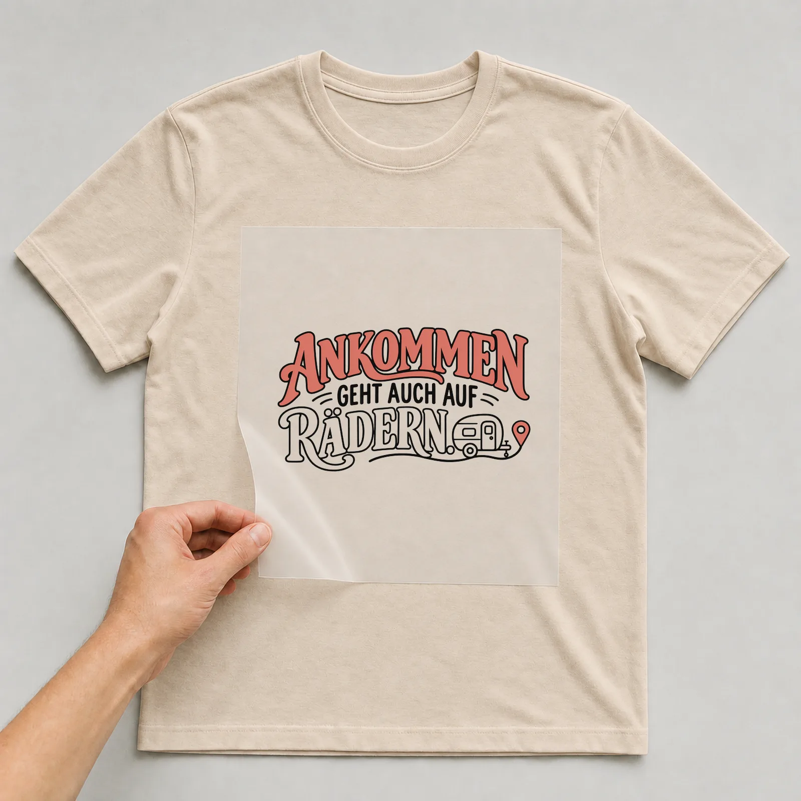 Bügelbild „Ankommen geht auch auf Rädern“ auf beigem T-Shirt, Folie wird aufgelegt