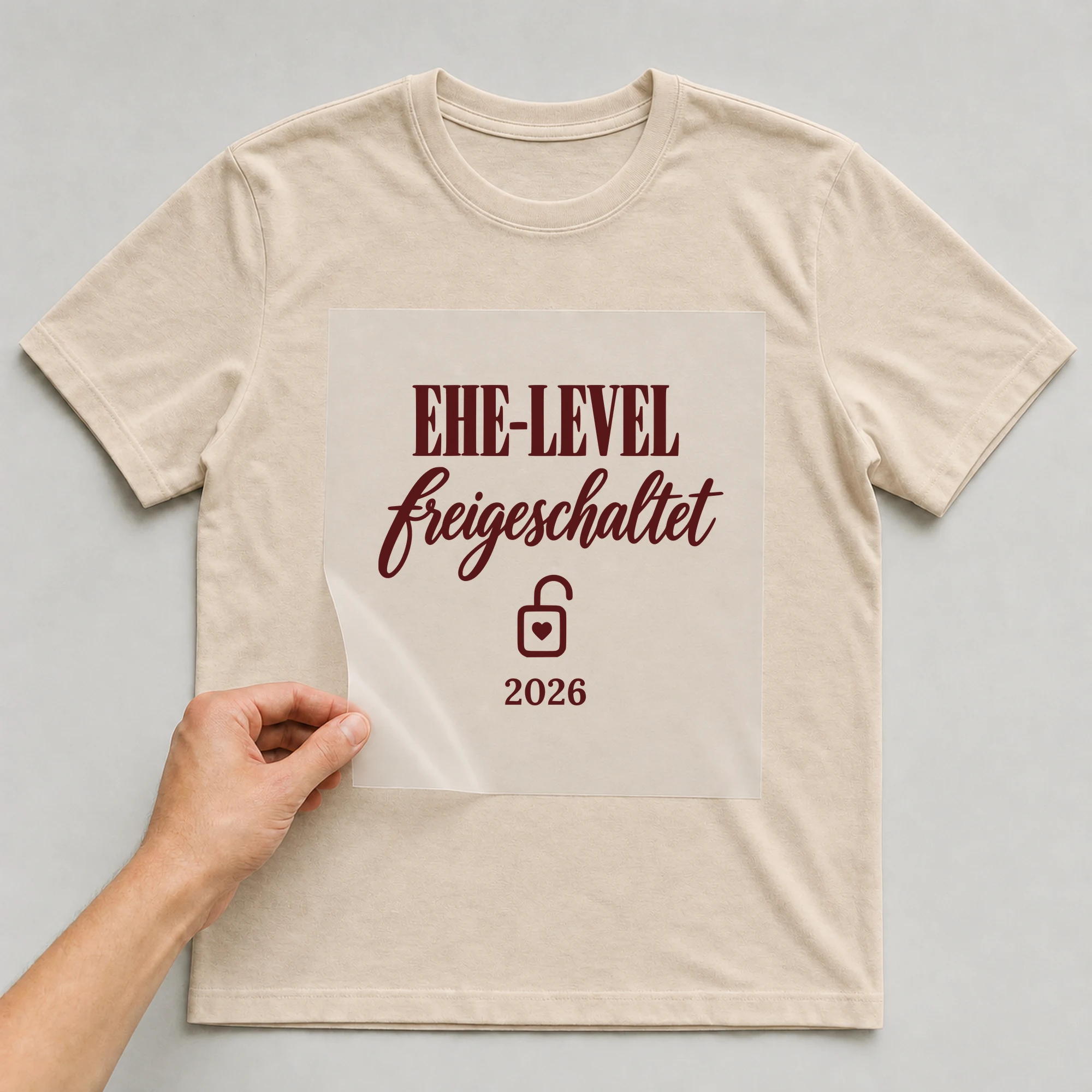 Bügelbild Ehe-Level freigeschaltet mit Jahr auf beigem T-Shirt, Folie wird aufgelegt