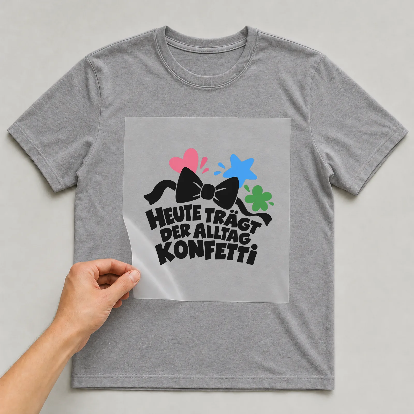 Bügelbild „Heute trägt der Alltag Konfetti“ auf grauem T-Shirt, Folie wird aufgelegt