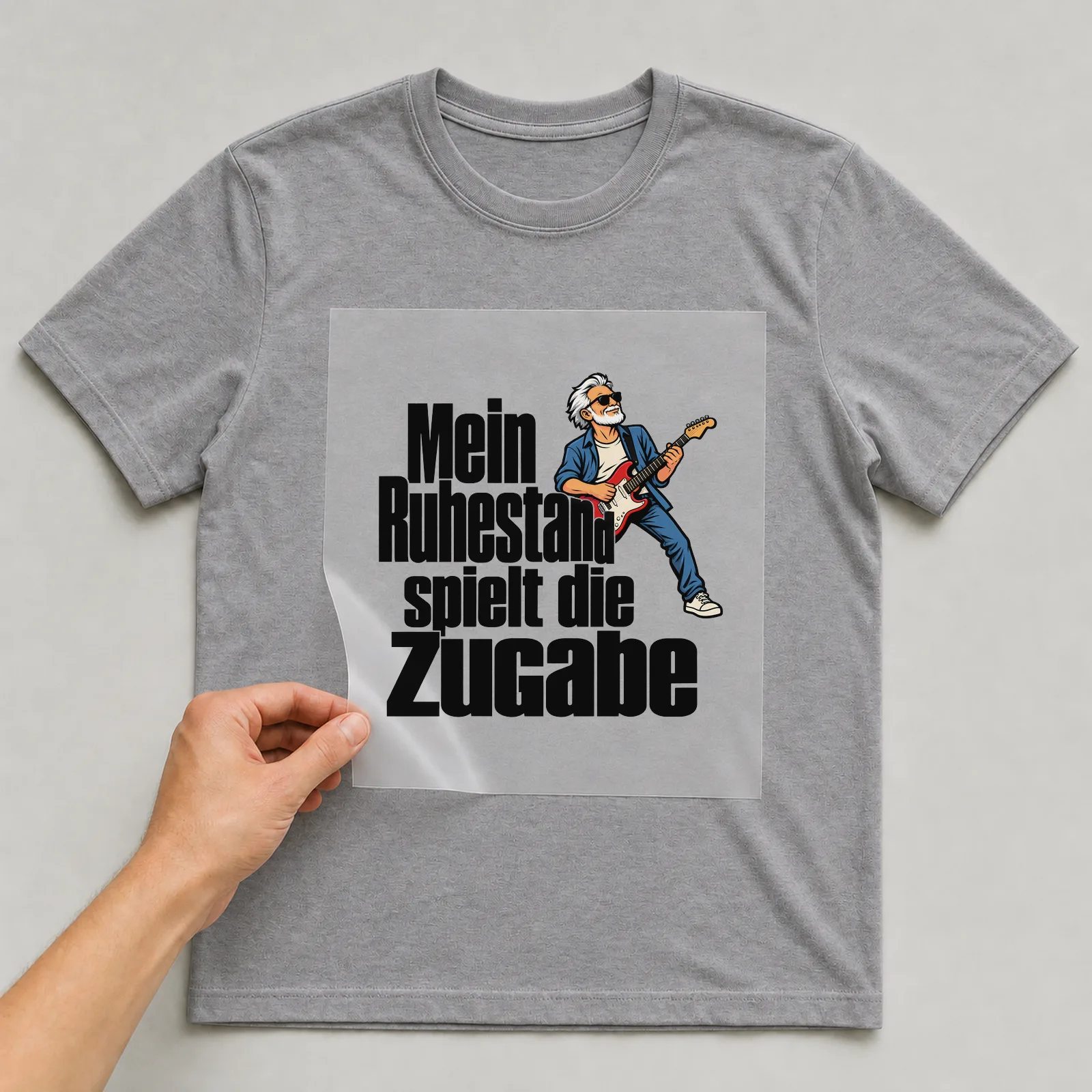 Bügelbild „Mein Ruhestand spielt die Zugabe“ auf grauem T-Shirt, Folie wird aufgelegt