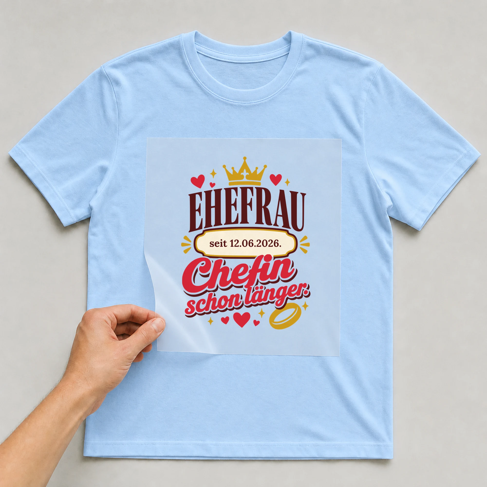 Bügelbild Ehefrau. Chefin schon länger. mit Datum auf hellblauem T-Shirt, Folie wird aufgelegt
