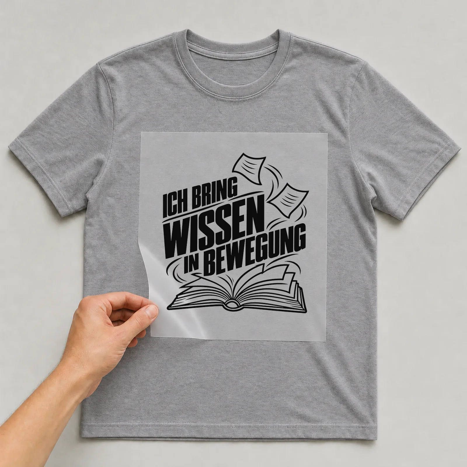 Bügelbild „Ich bring Wissen in Bewegung“ auf grauem T-Shirt, Folie wird aufgelegt