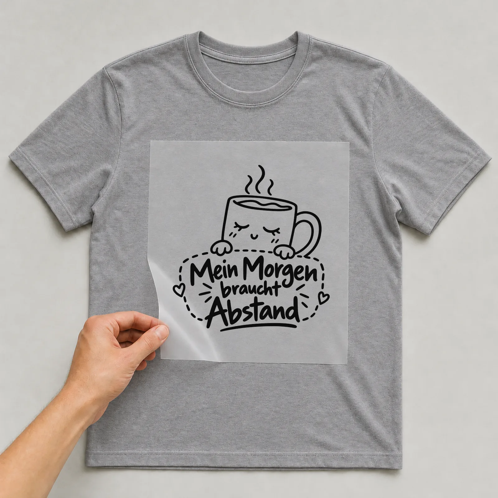Bügelbild „Mein Morgen braucht Abstand“ auf grauem T-Shirt, Folie wird aufgelegt