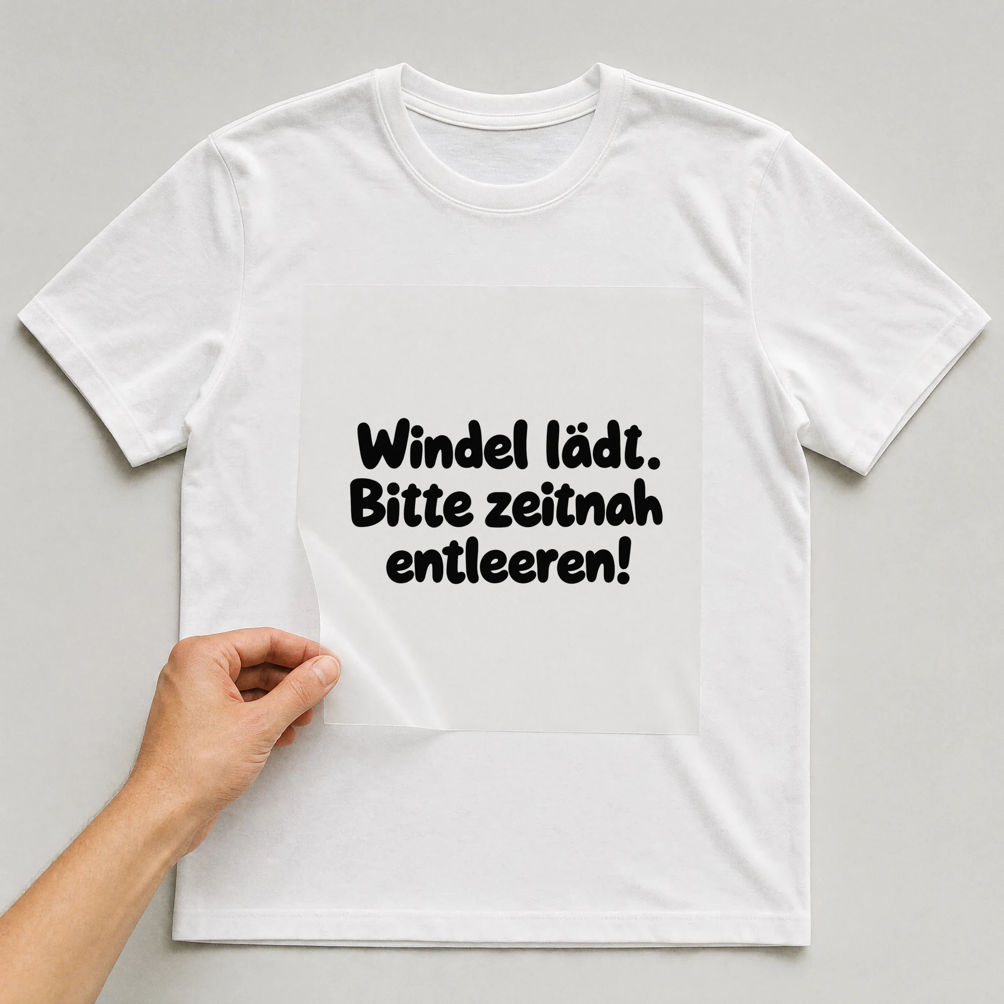Bügelbild „Windel lädt. Bitte zeitnah entleeren!“ auf weißem T-Shirt, Folie wird aufgelegt