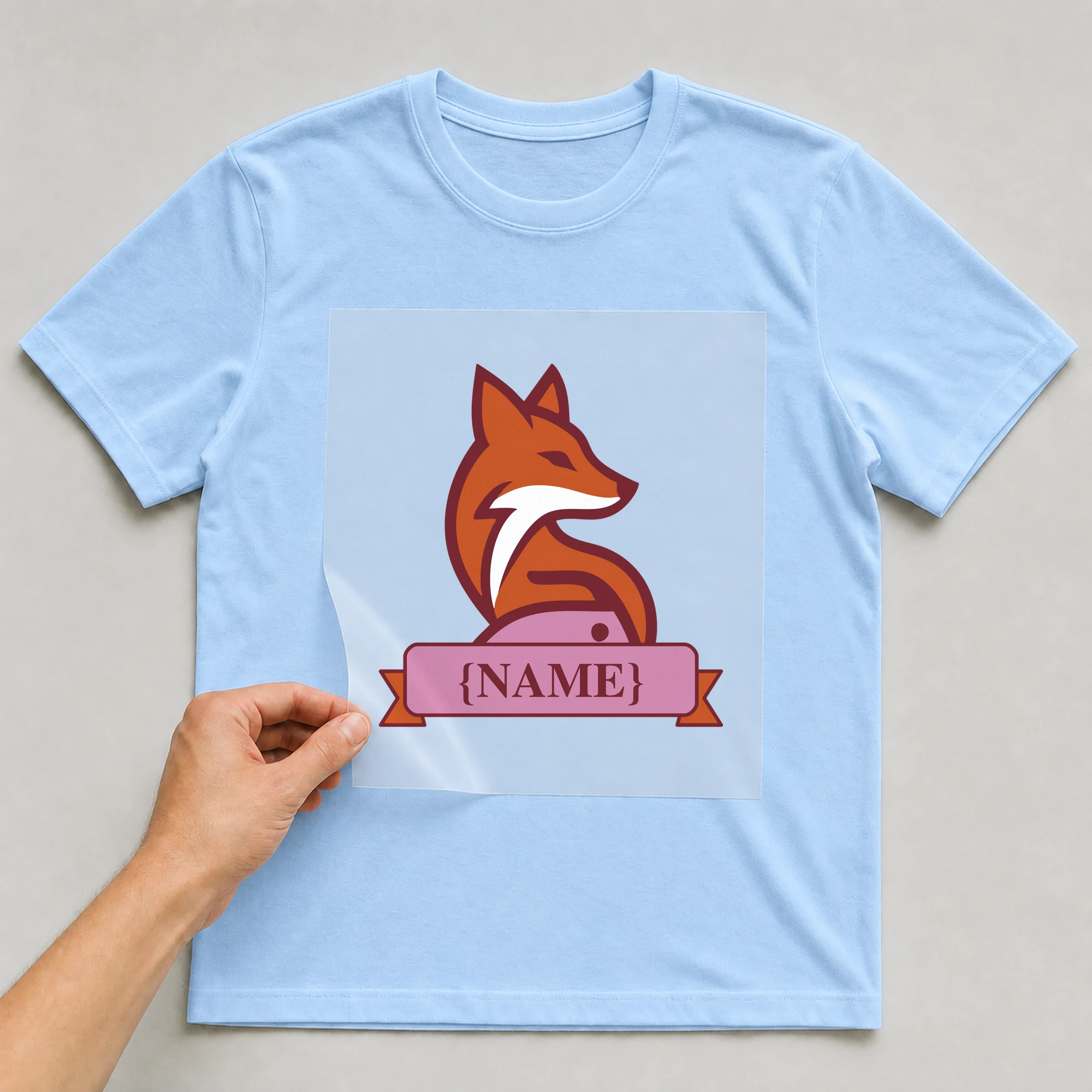 Bügelbild „Namensschild Fuchs“ auf babyblauem T-Shirt, Folie wird aufgelegt