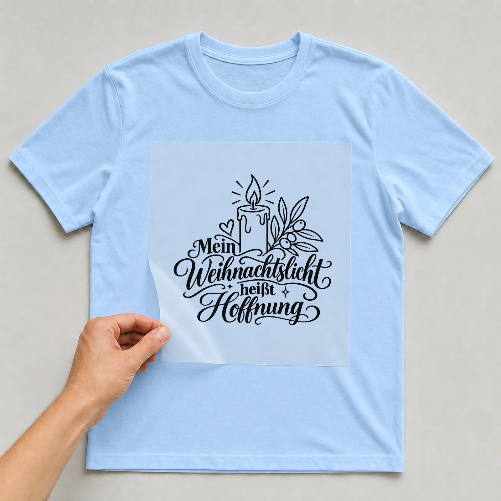 Bügelbild „Mein Weihnachtslicht heißt Hoffnung“ auf hellblauem T-Shirt, Folie wird aufgelegt