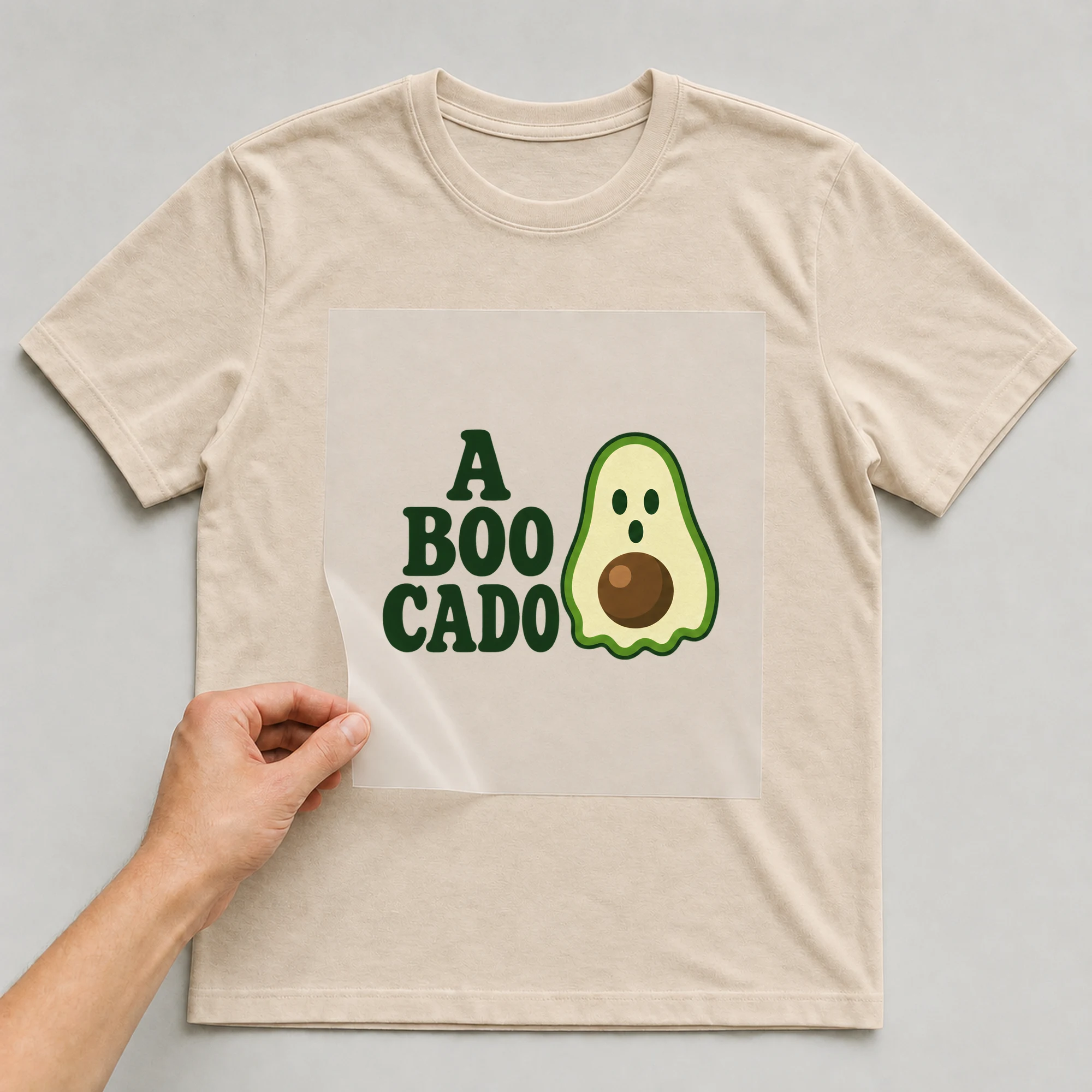 Bügelbild „A BOO CADO“ auf beigem T-Shirt, Folie wird aufgelegt