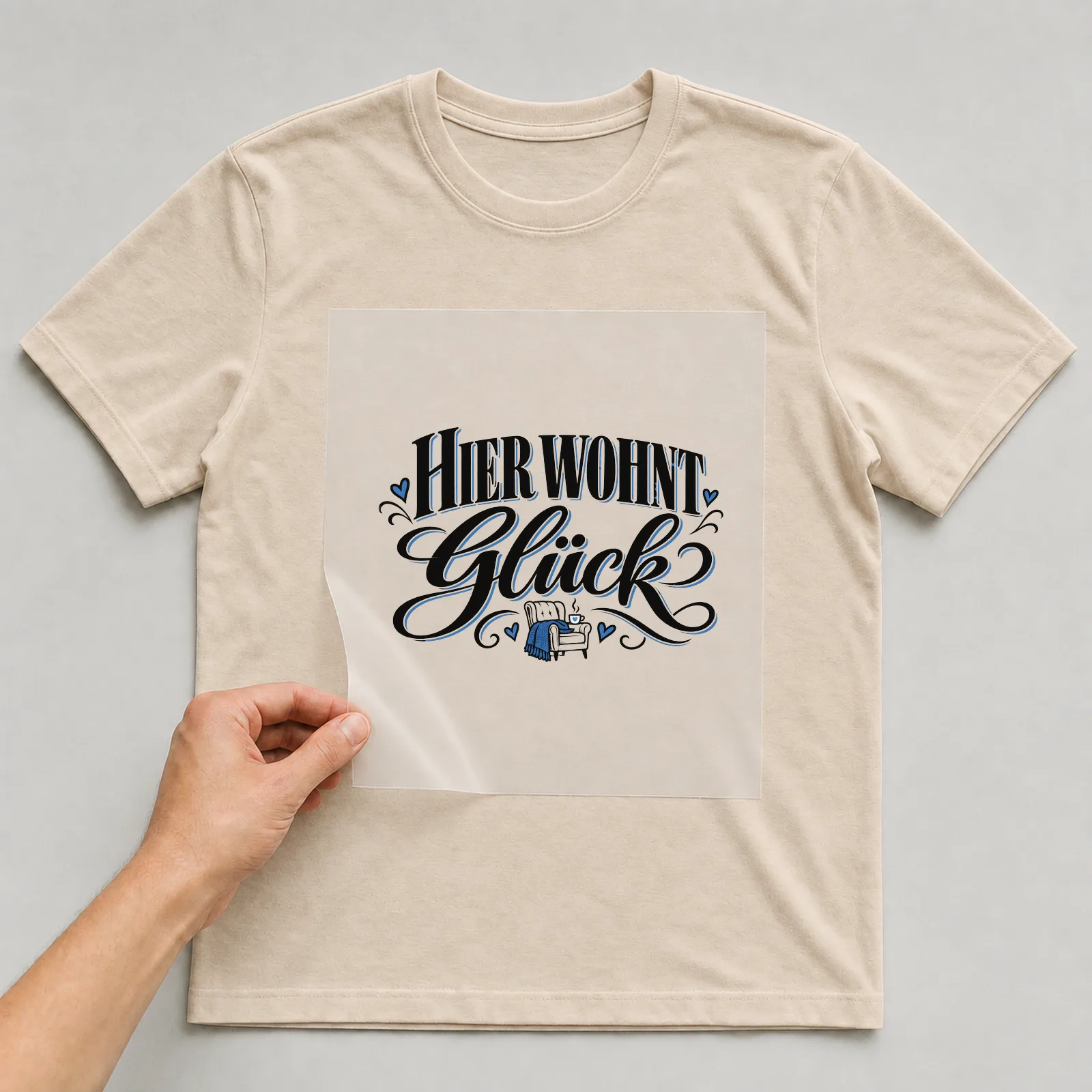 Bügelbild „Hier wohnt Glück“ auf beigem T-Shirt, Folie wird aufgelegt