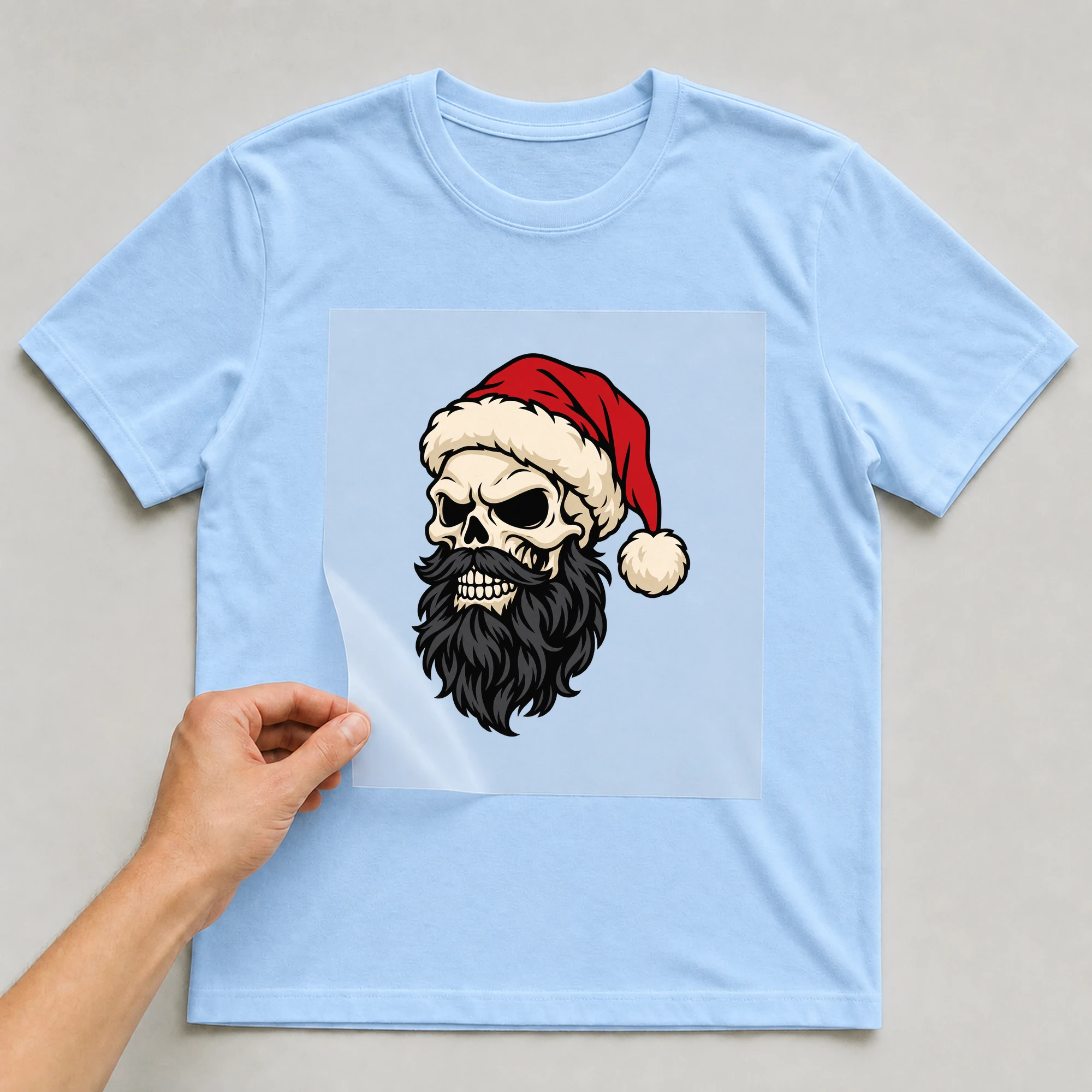 Bügelbild „Bad Santa Skull Beard“ auf babyblauem T-Shirt, Folie wird aufgelegt