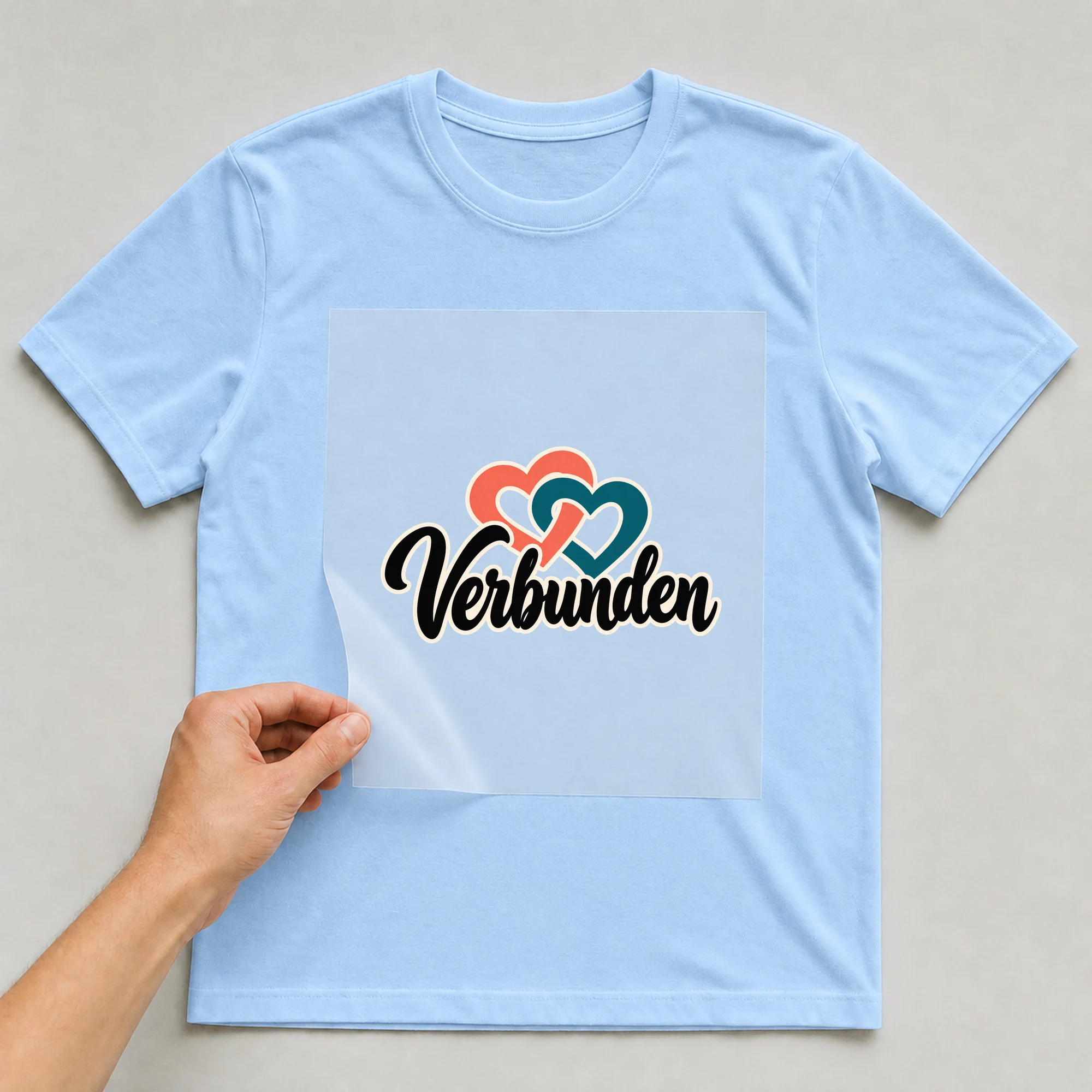 Bügelbild „Verbunden“ auf babyblauem T-Shirt, Folie wird aufgelegt