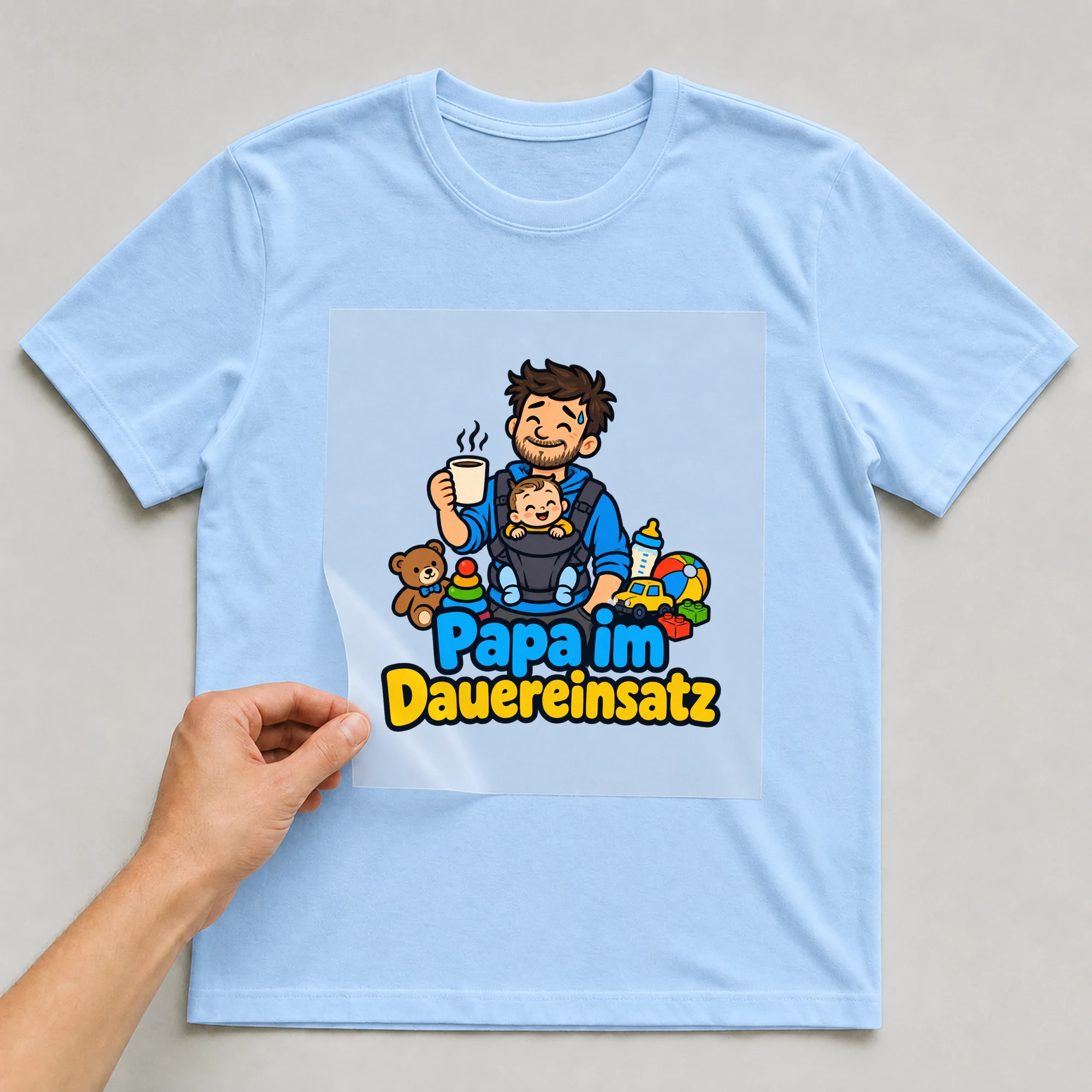 Bügelbild „Papa im Dauereinsatz“ auf babyblauem T-Shirt, Folie wird aufgelegt