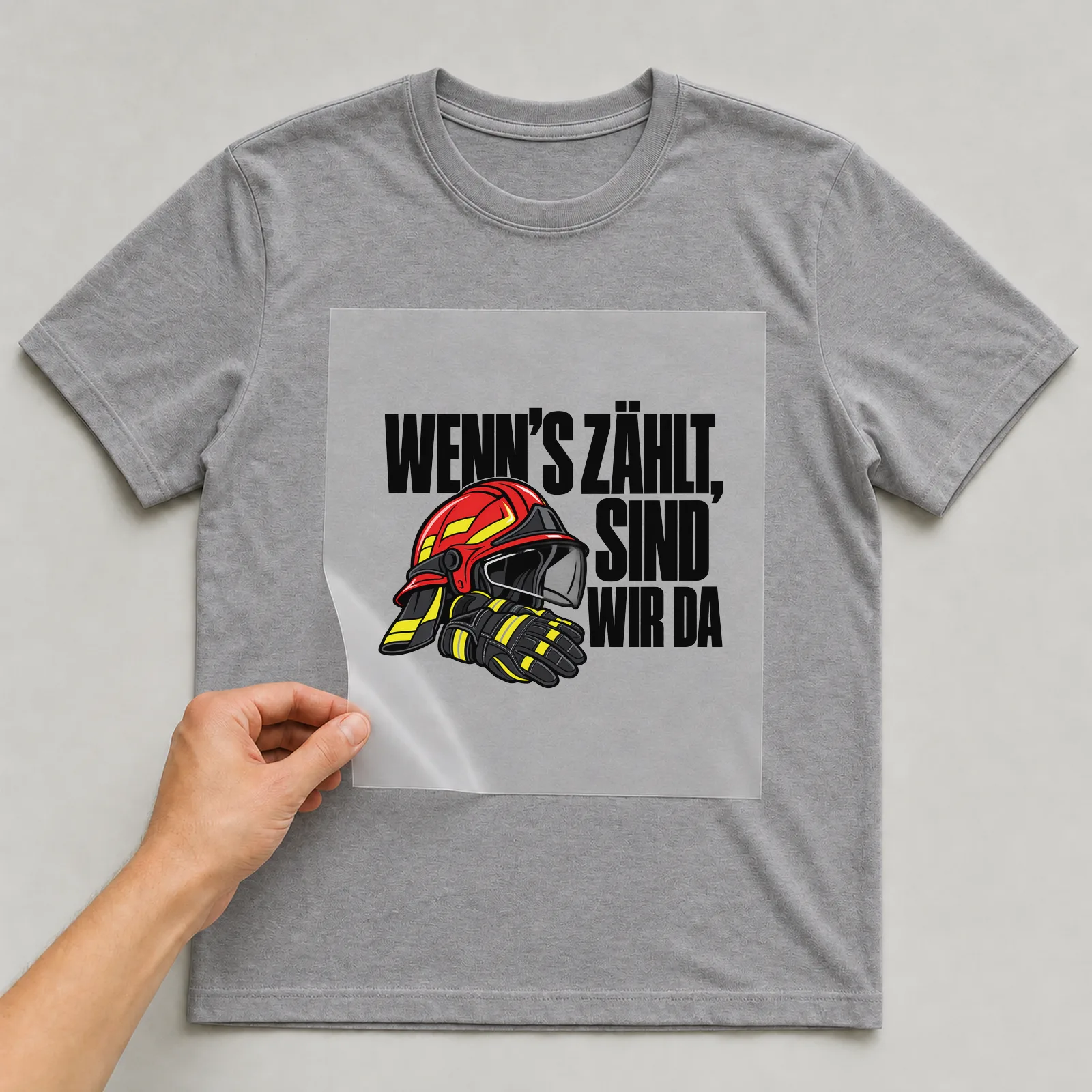 Bügelbild „Wenn’s zählt, sind wir da“ auf grauem T-Shirt, Folie wird aufgelegt