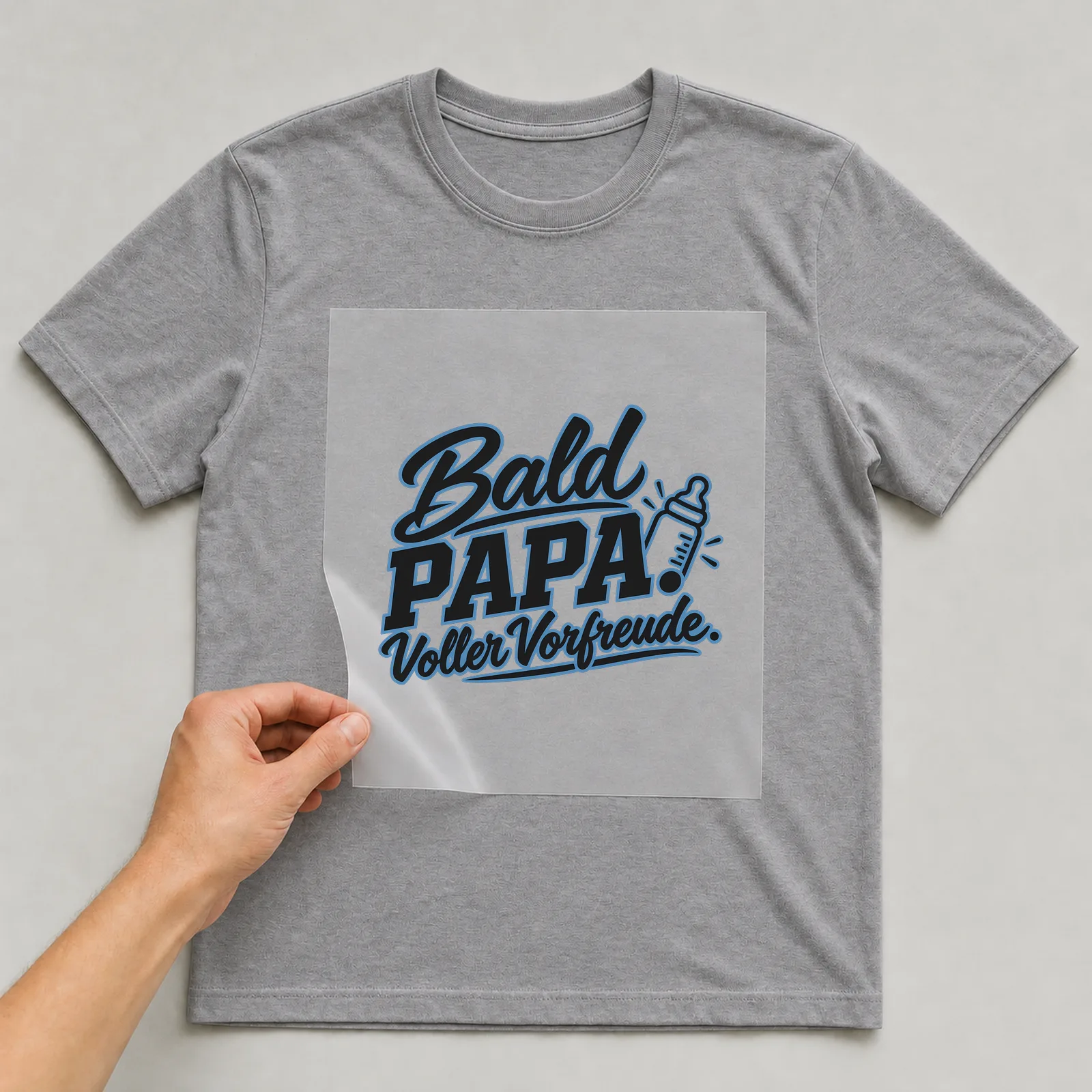 Bügelbild „Bald Papa. Voller Vorfreude.“ auf grauem T-Shirt, Folie wird aufgelegt
