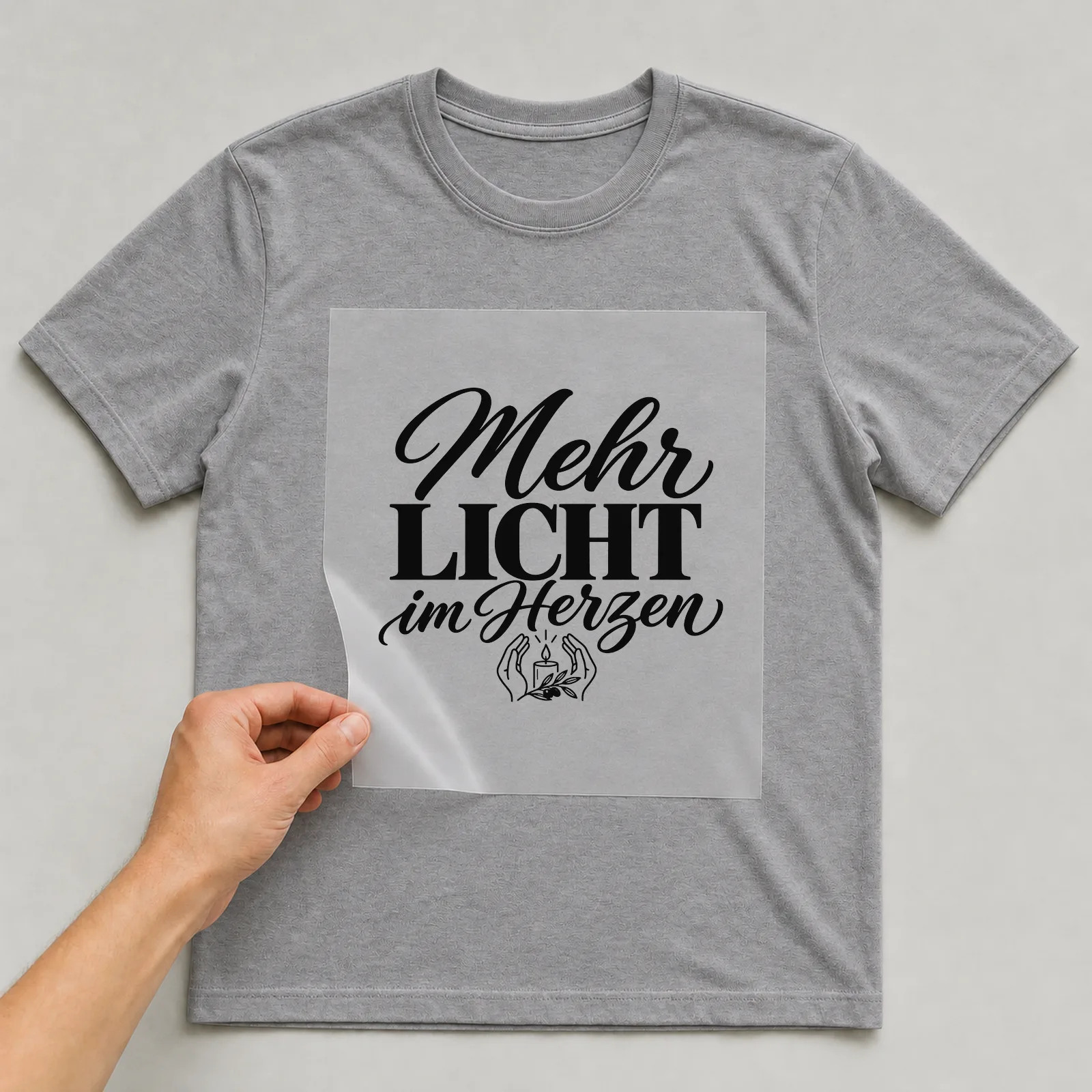Bügelbild „Mehr Licht im Herzen“ auf grauem T-Shirt, Folie wird aufgelegt