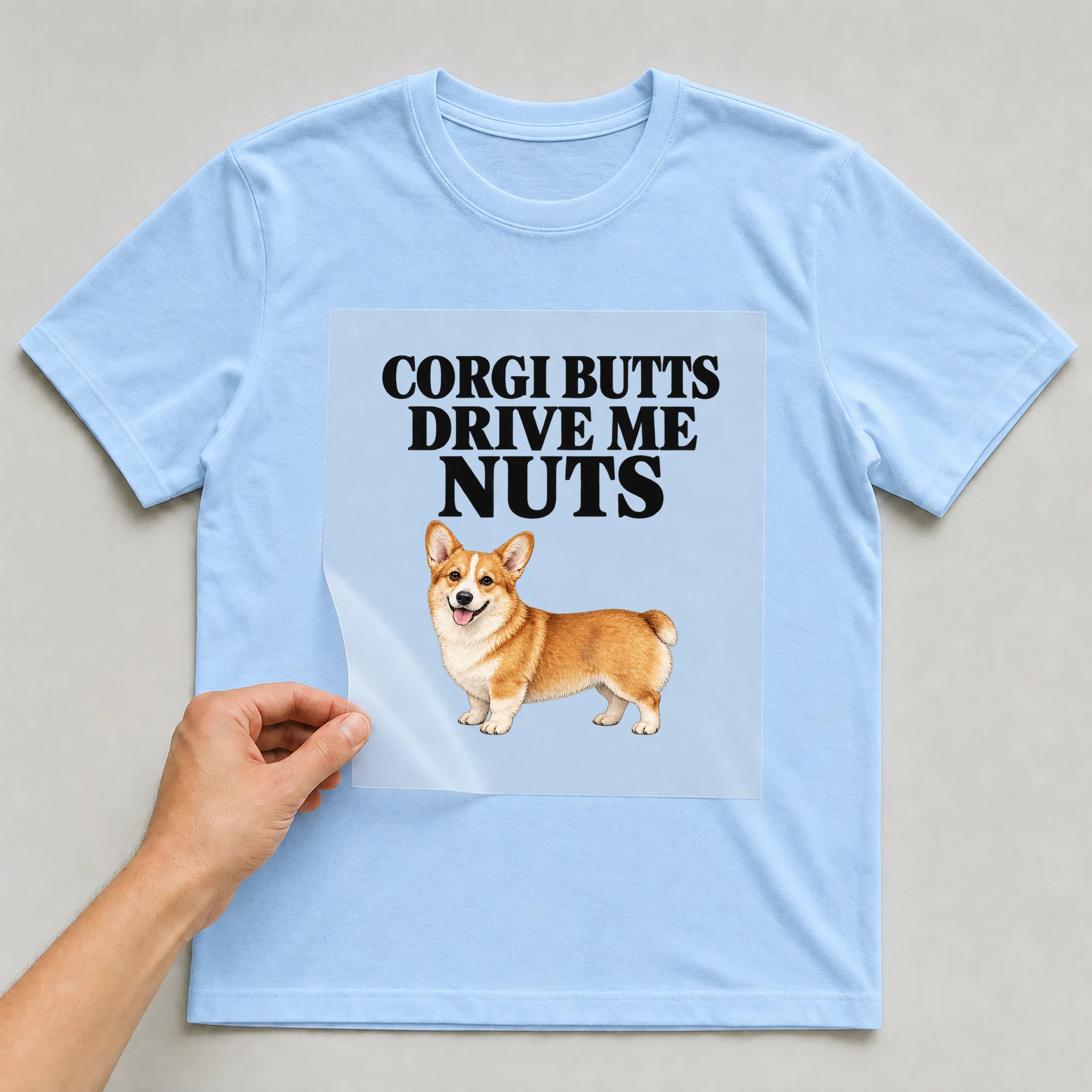Bügelbild „CORGI BUTTS DRIVE ME NUTS“ auf babyblauem T-Shirt, Folie wird aufgelegt