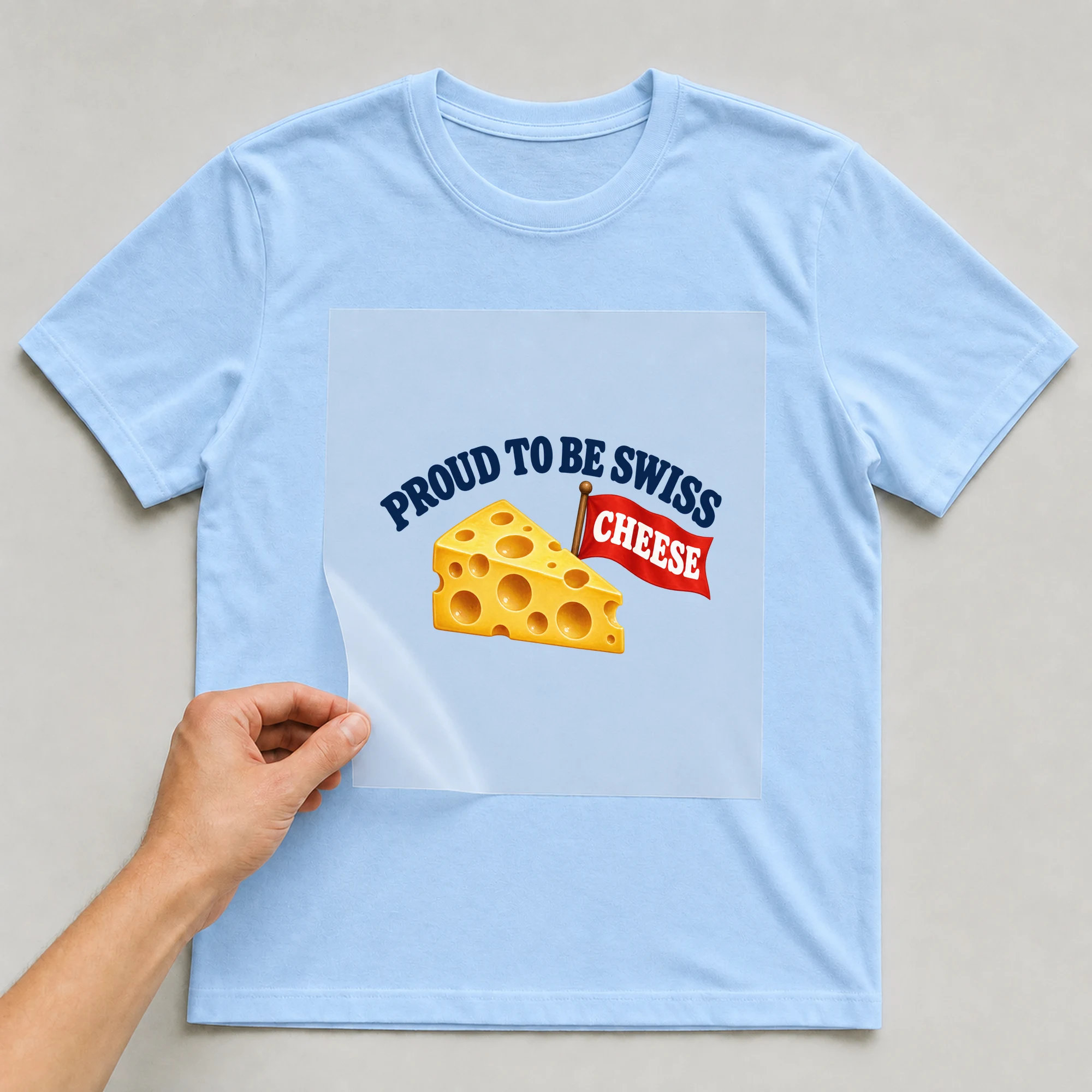 Bügelbild „Proud To Be Swiss Cheese“ auf babyblauem T-Shirt, Folie wird aufgelegt